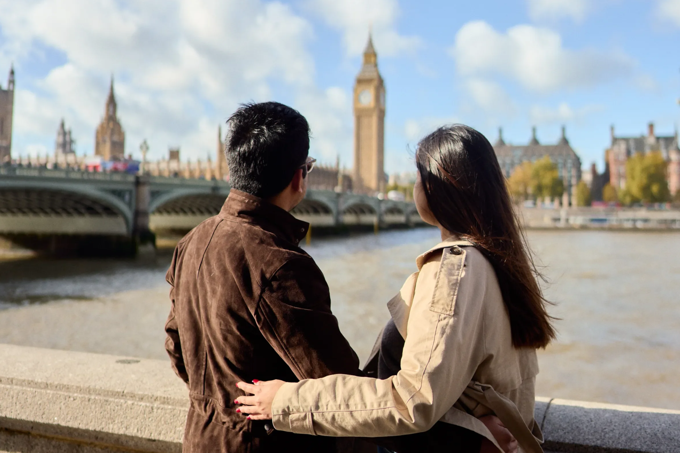 Couple seen from behind with arms around each other looking towards Big Ben and Westminster Bridge from the South Bank, London