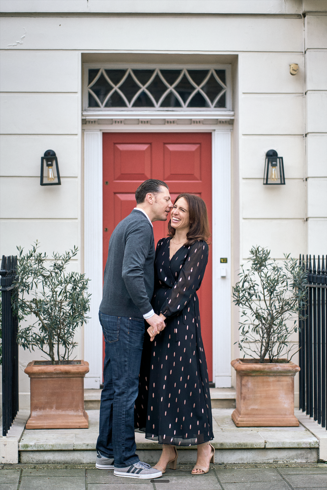Couple sharing a moment outside a red door on a white stucco London terrace — couples photography by Tepewehco
