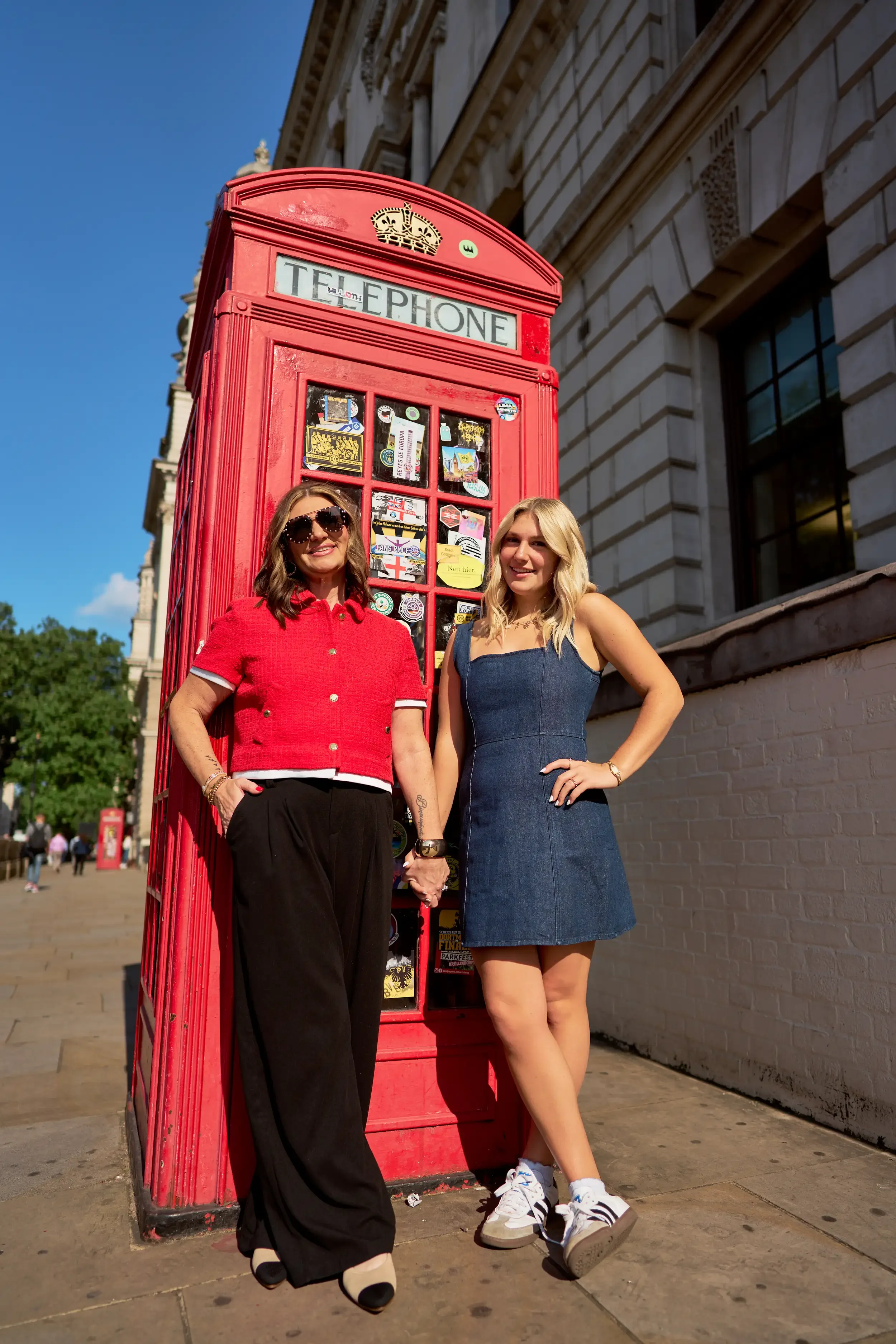 Mother and daughter posing together next to a red London telephone box near Westminster during a family photoshoot, London