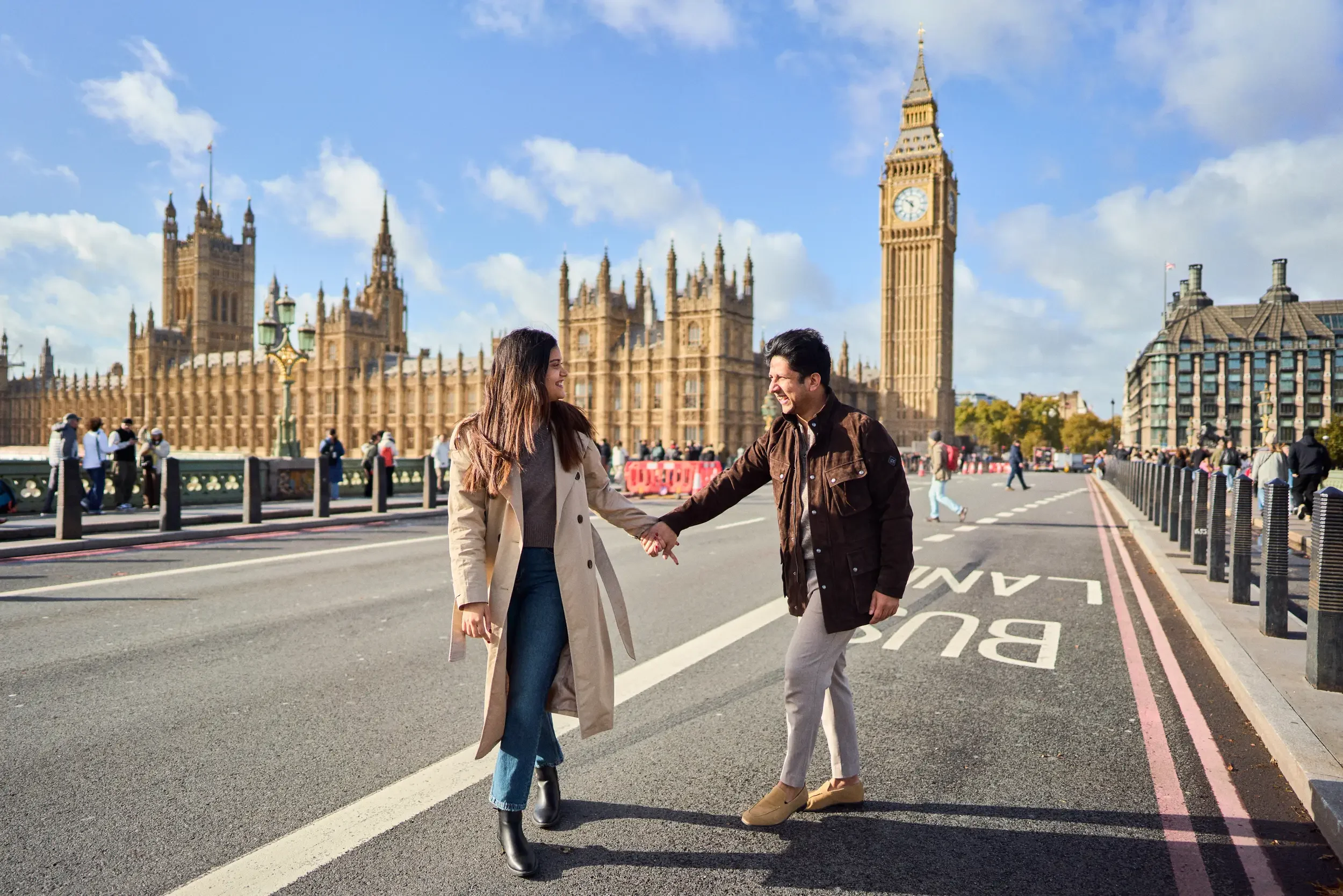 Couple laughing and holding hands on Westminster Bridge with Big Ben and the Houses of Parliament in the background, London