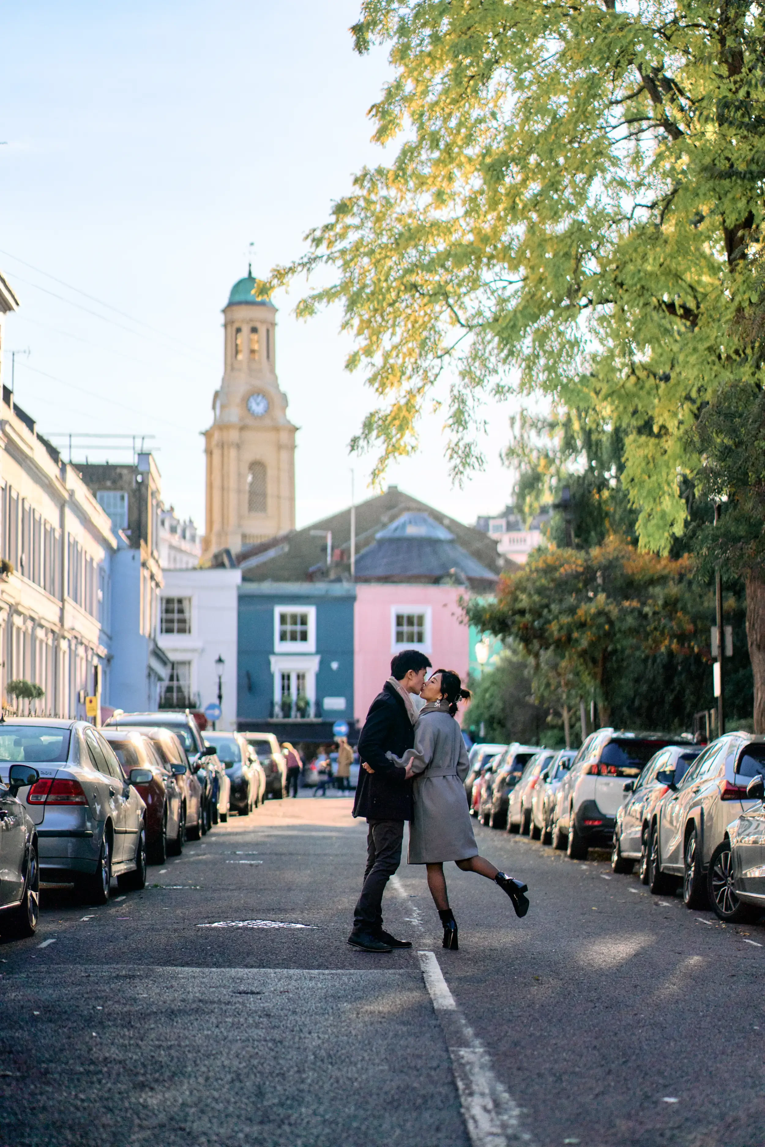 Couple kissing in the middle of Notting Hill Portobello road with colourful pastel houses and a church tower in the background, London - Tepewehco Photography by Kate