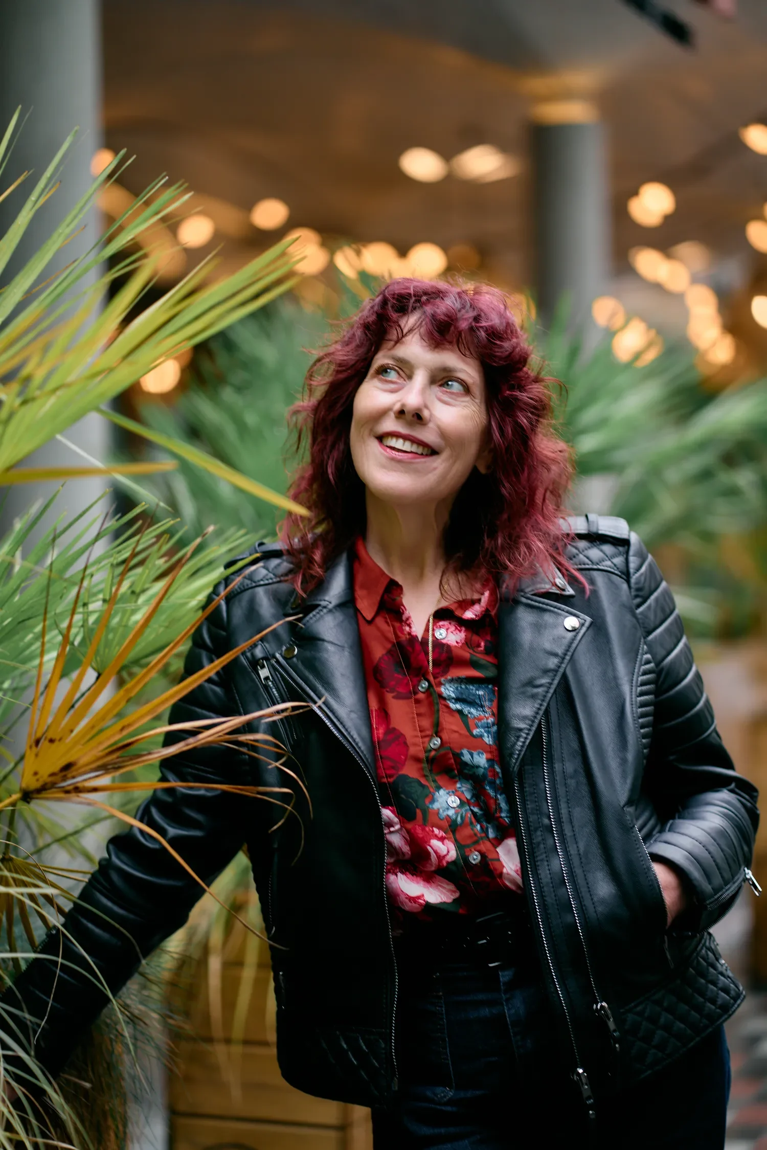 Woman with red hair in a leather jacket laughing under warm bokeh lights in Covent Garden