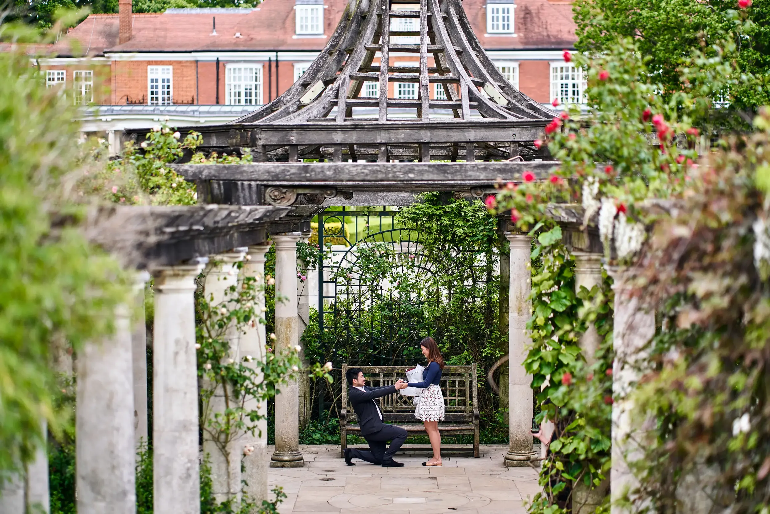 Man proposing under a rose-covered wooden gazebo in the Hampstead Heath pergola garden, London