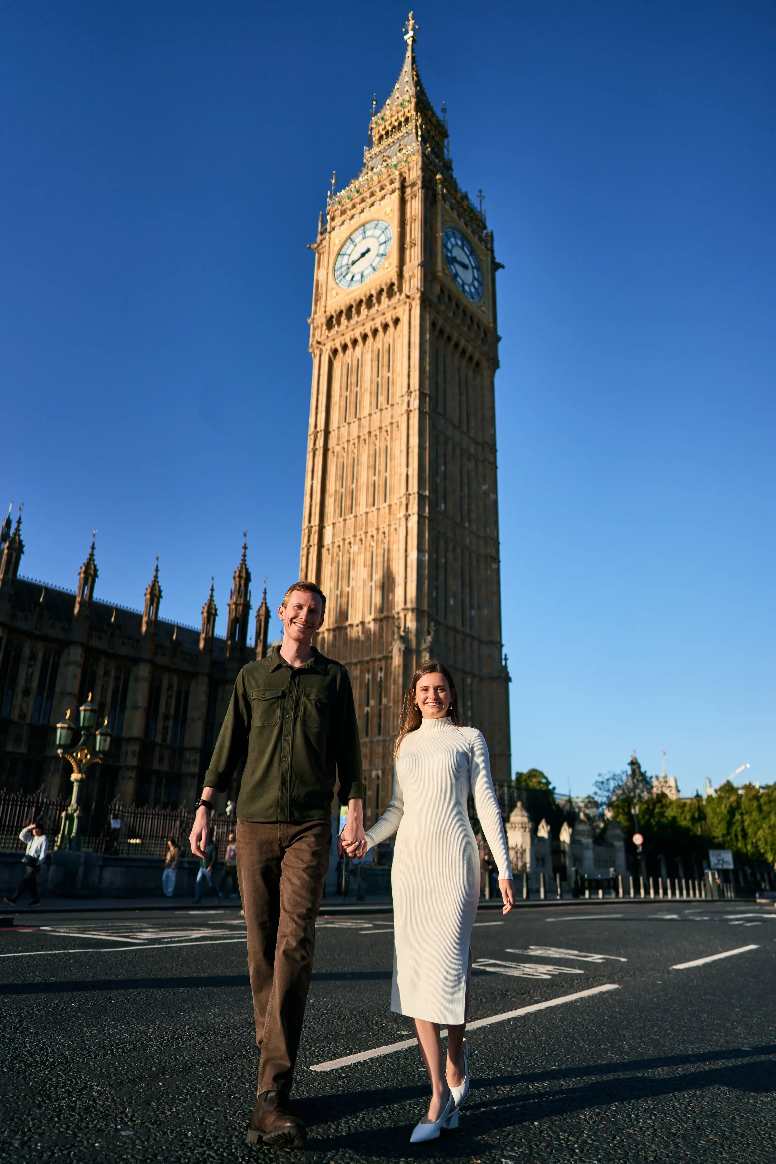 Couple walking hand in hand towards the camera with Big Ben towering behind them on a clear blue sky day in Westminster, London