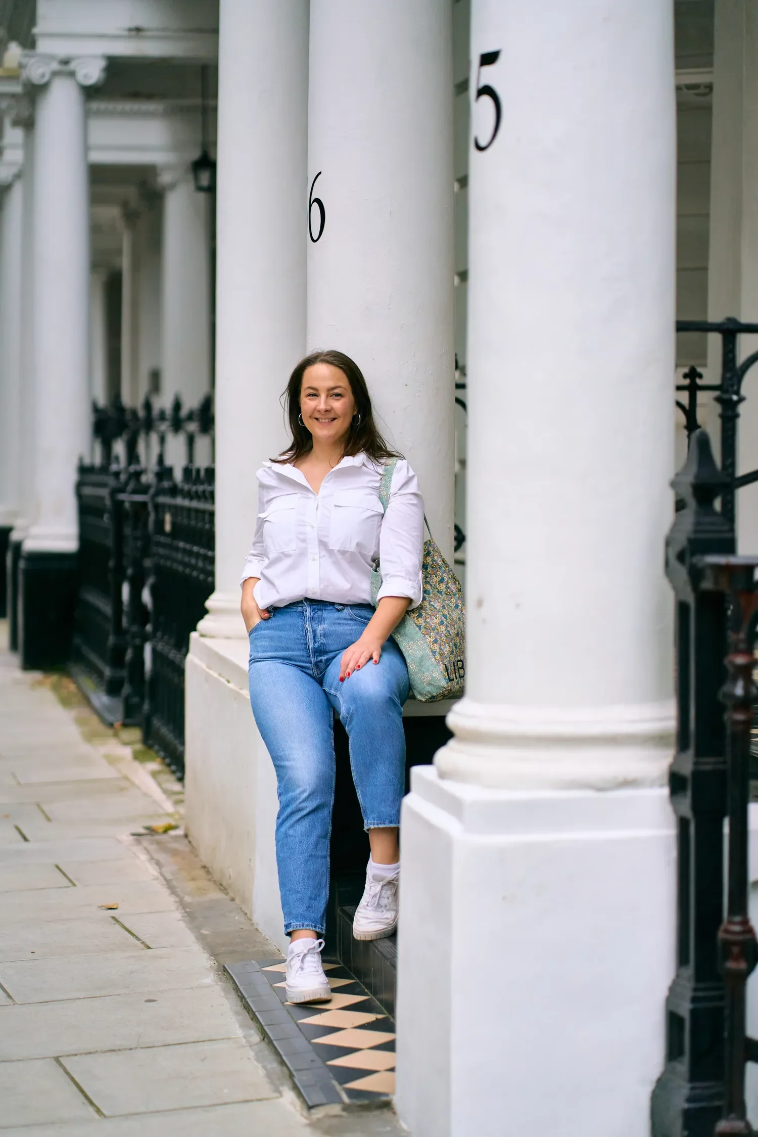 Woman in a white shirt and jeans leaning on a white column outside a Chelsea townhouse