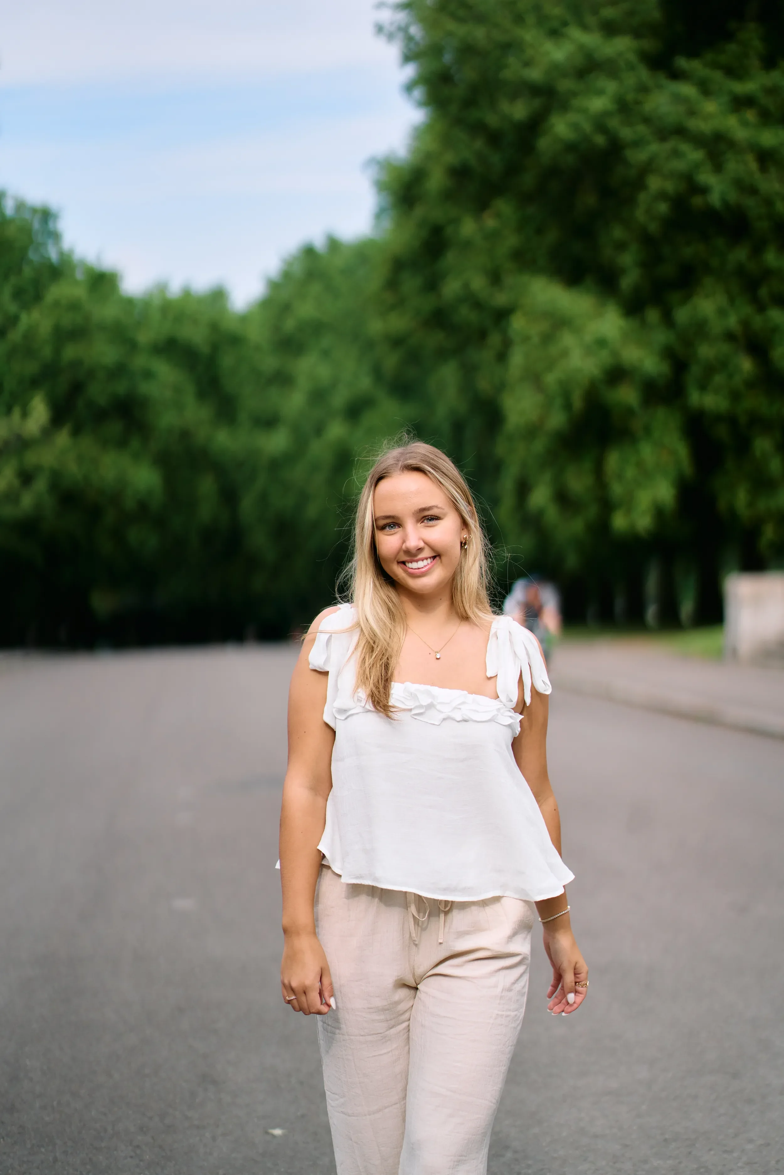 High school senior looking back over her shoulder while walking along a tree-lined avenue in Kensington Gardens, London