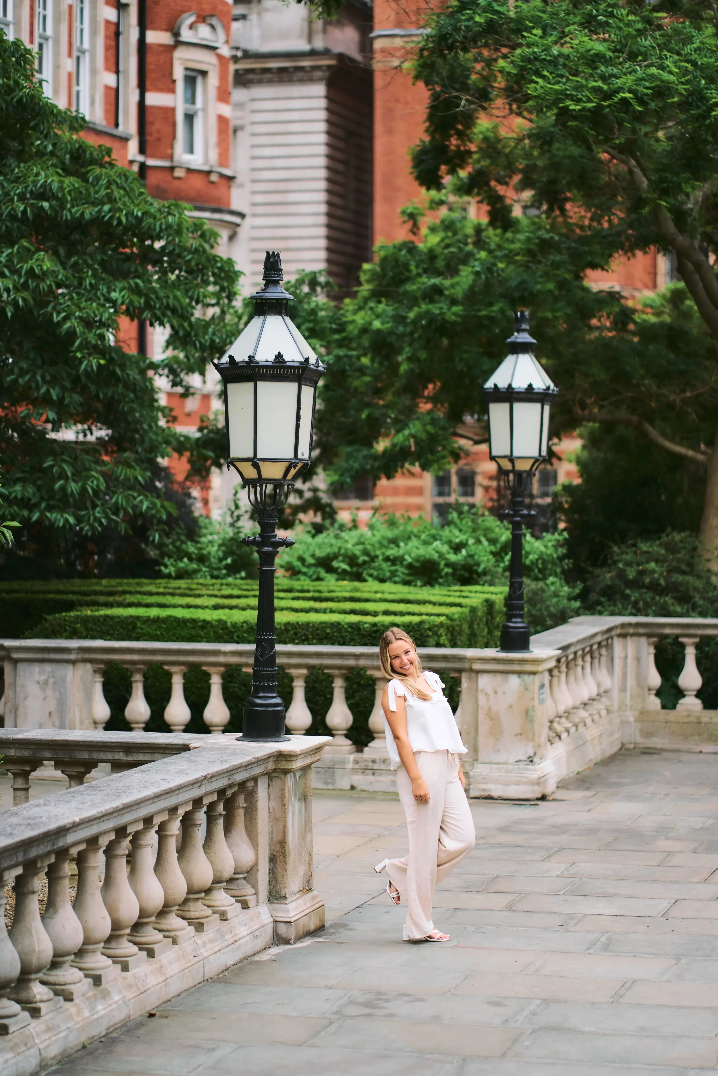 High school senior in a white dress on stone steps beside Victorian lamp posts in Kensington