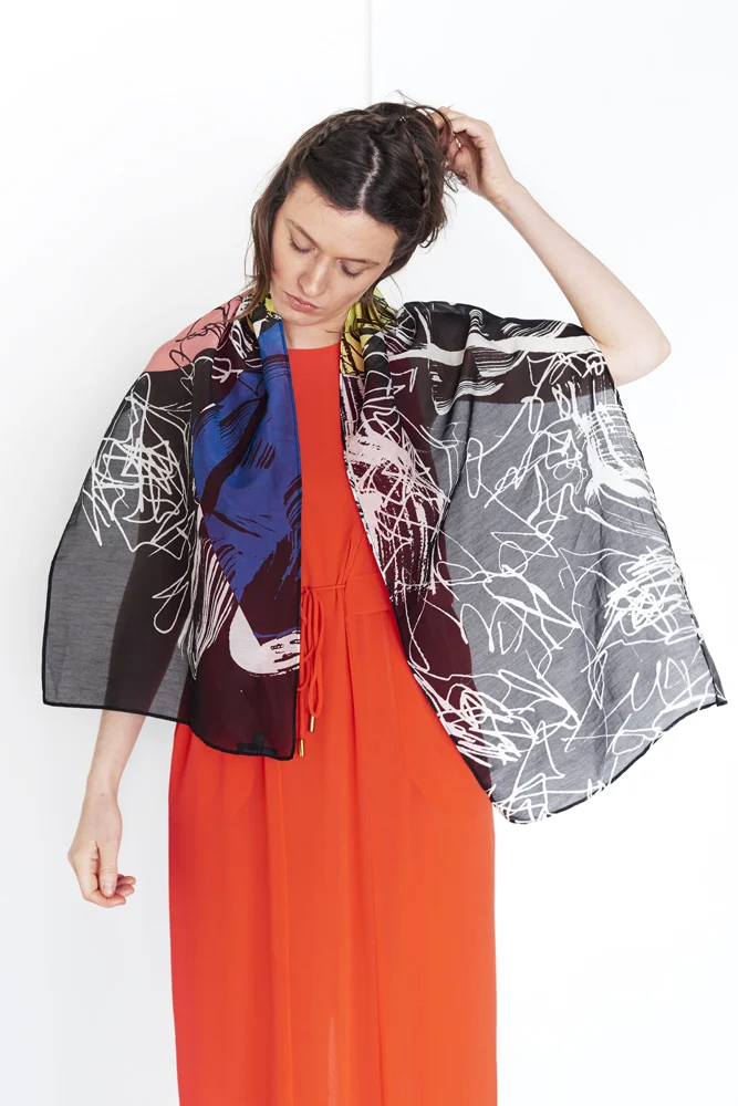 WOMAN IN A RED DRESS WITH A BLACK COTTON SILK SCARF WITH MULTI-COLOURED ABSTRACT PAINTERLY PATTERN DRAPED OVER HER NECK