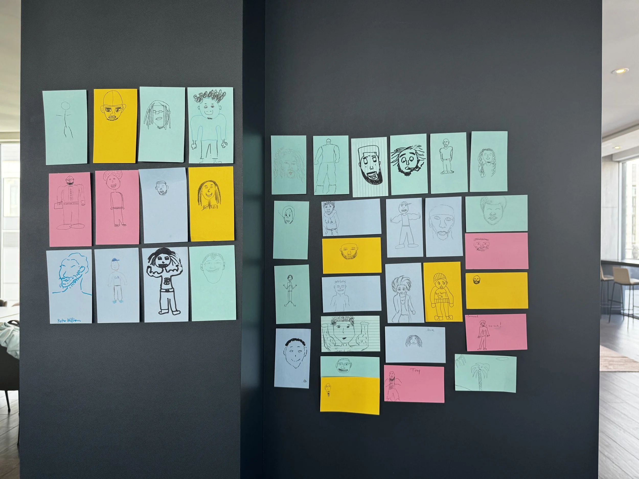 Different coloured paper on a black wall with drawings of various cartoon men.