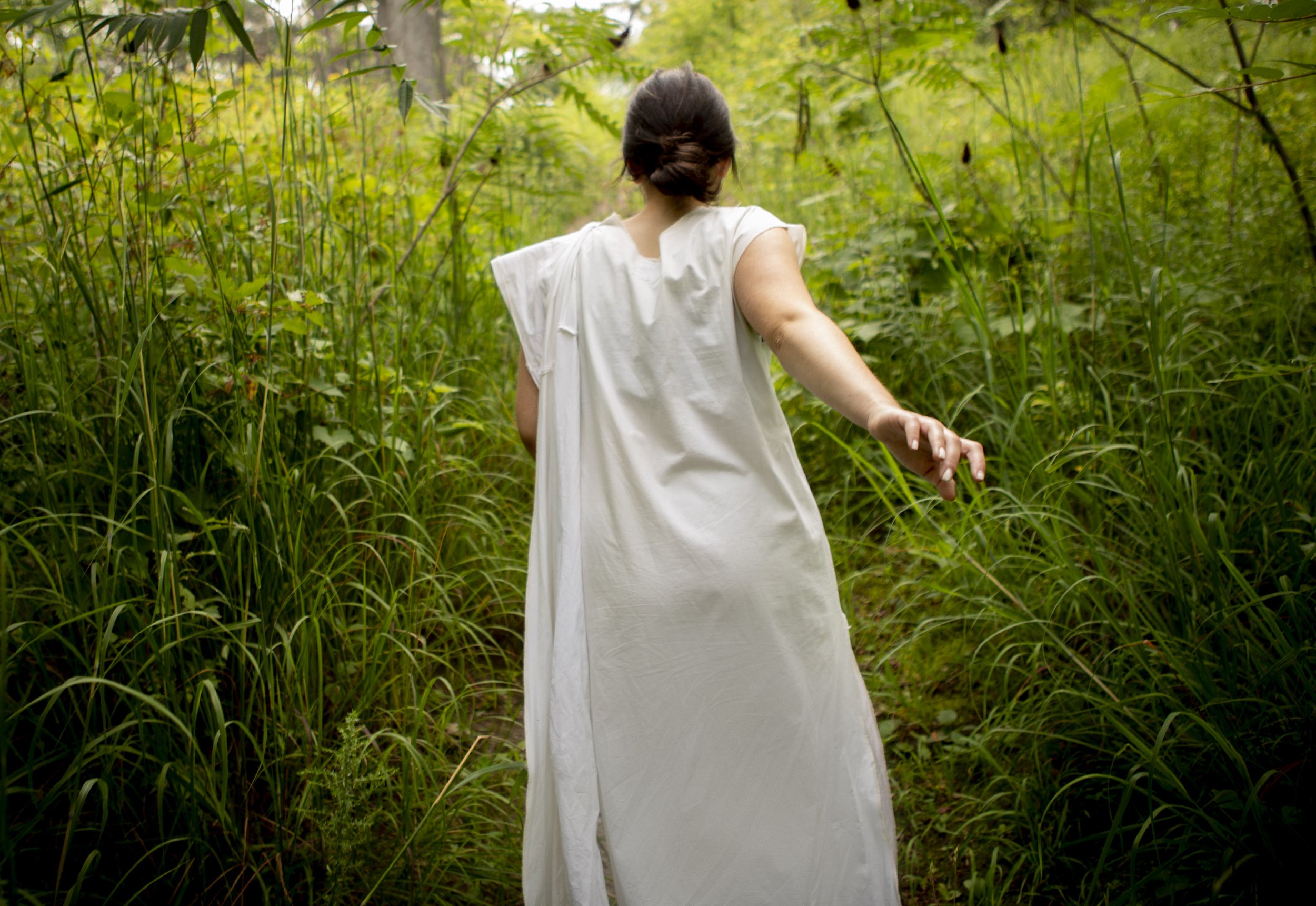 Woman in a white frock walking in a field of tall grass.