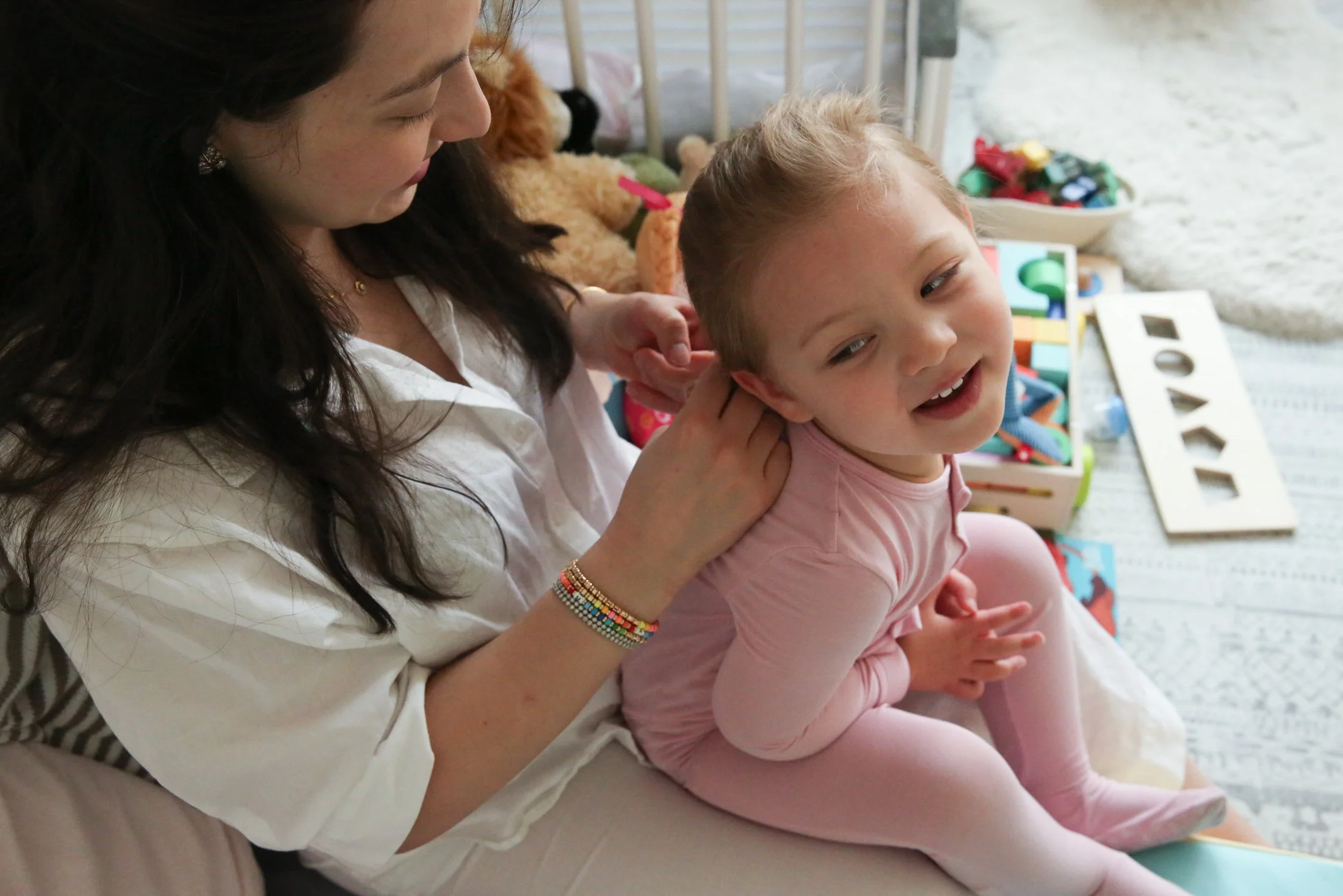 Toddler girl sitting on mother's lap while mother braids her hair 