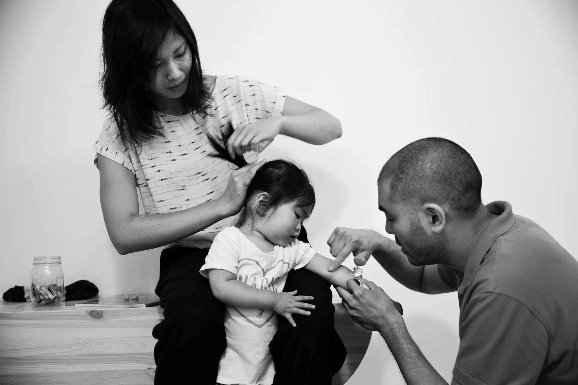 Woman puts girl's hair in a ponytail while man dabs ointment on girl's arm