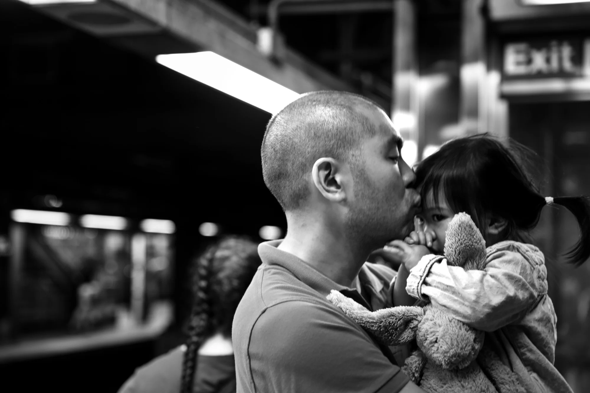 Man kisses girl on her forehead while she holds a stuffed bunny and sucks her thumb