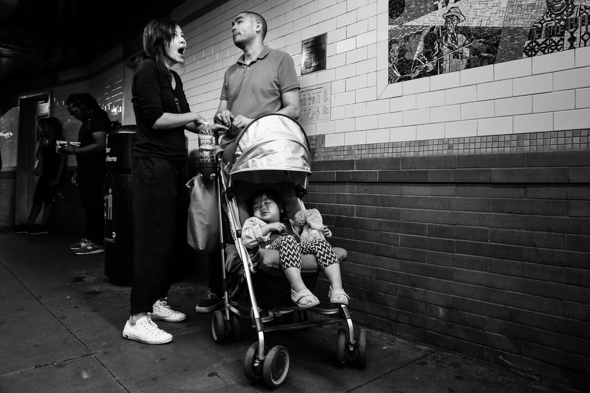 Girl sleeps in stroller while man stands and woman yawns