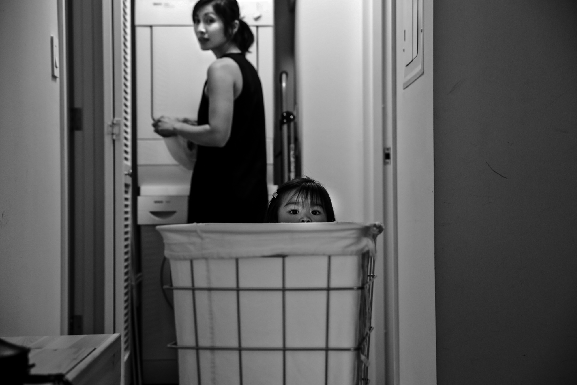 Girl peeks out behind laundry basket while woman looks