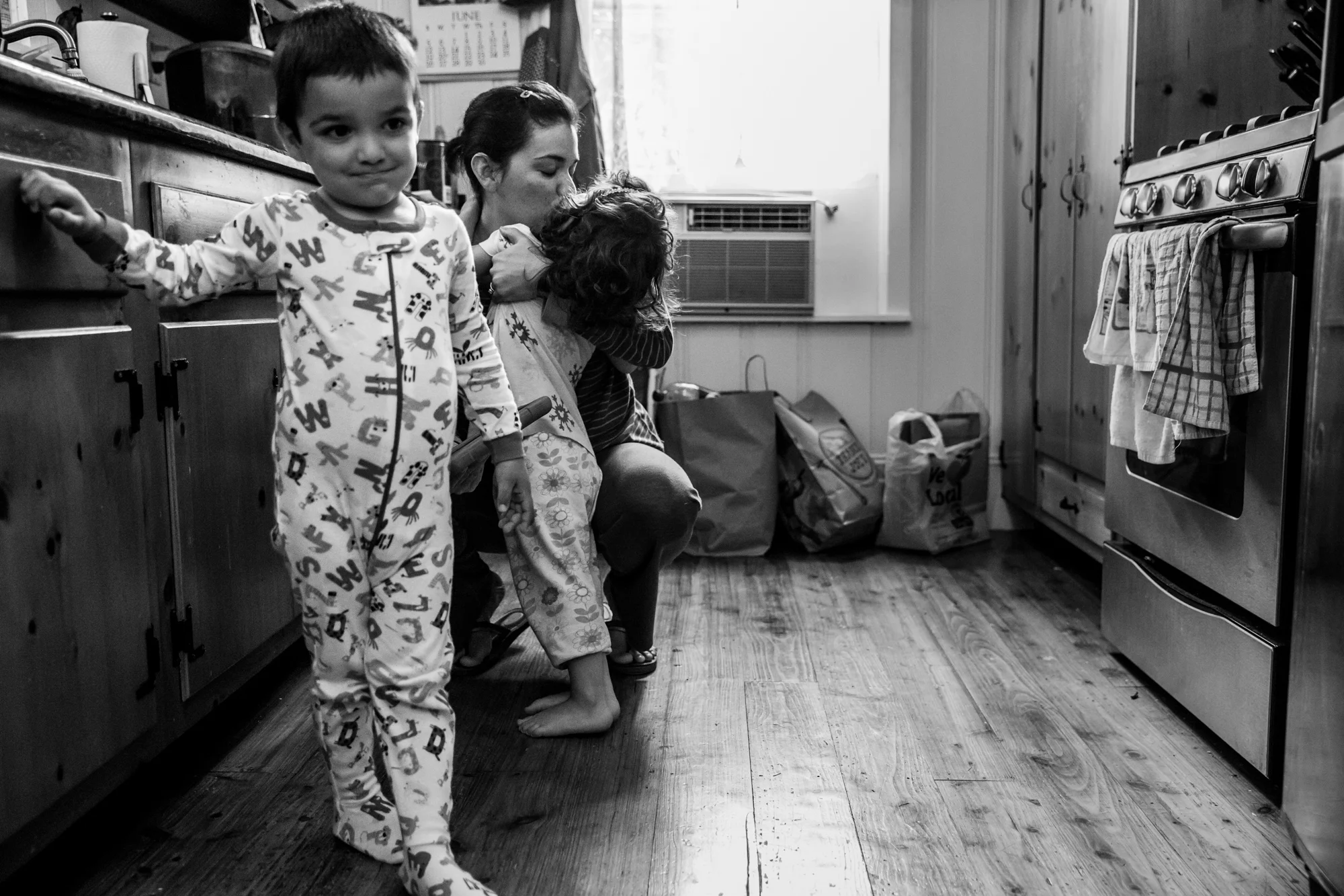 Boy stands by cabinet while girl kisses mother