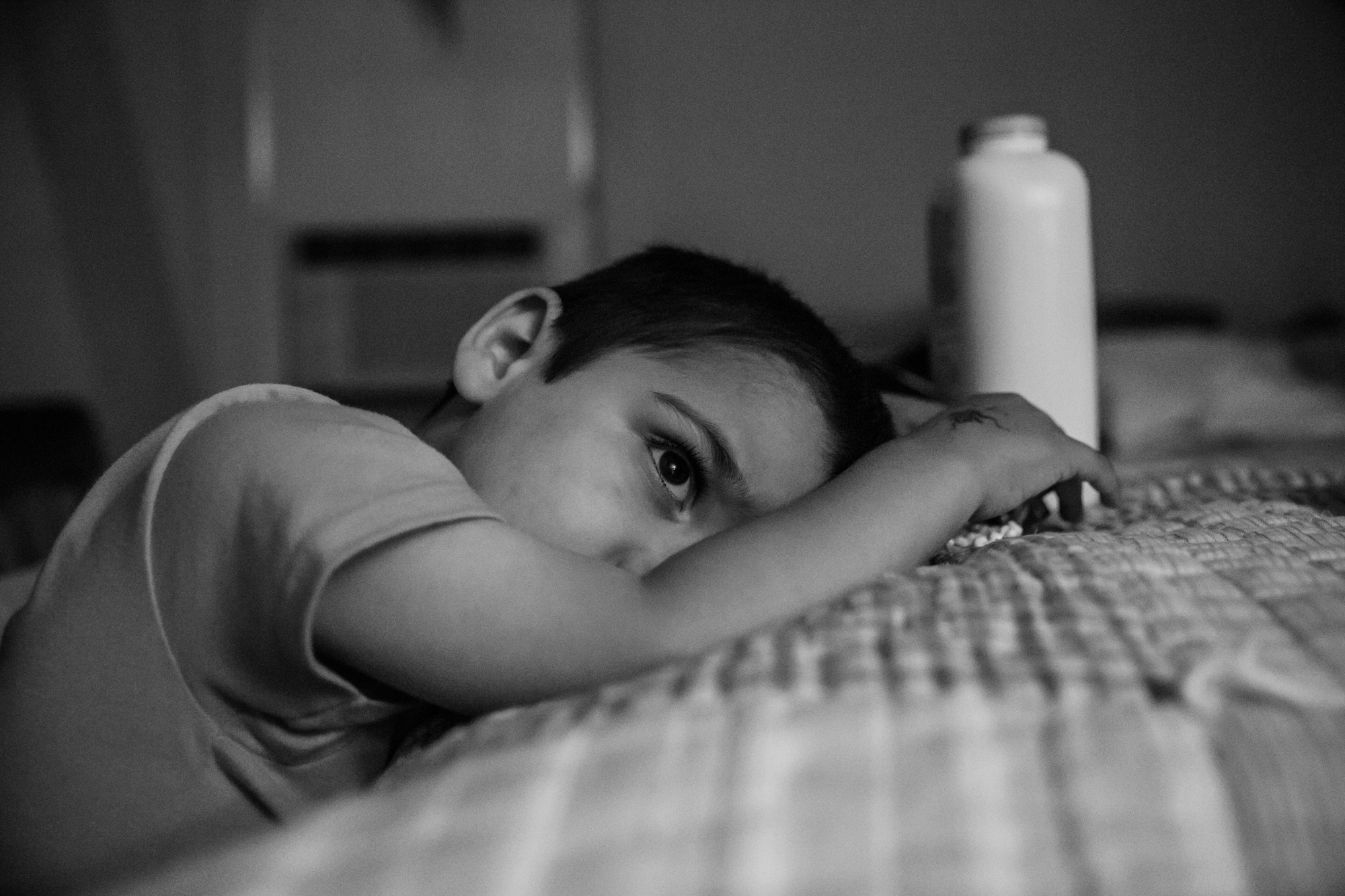 Tired boy leans on bed with a white bottle