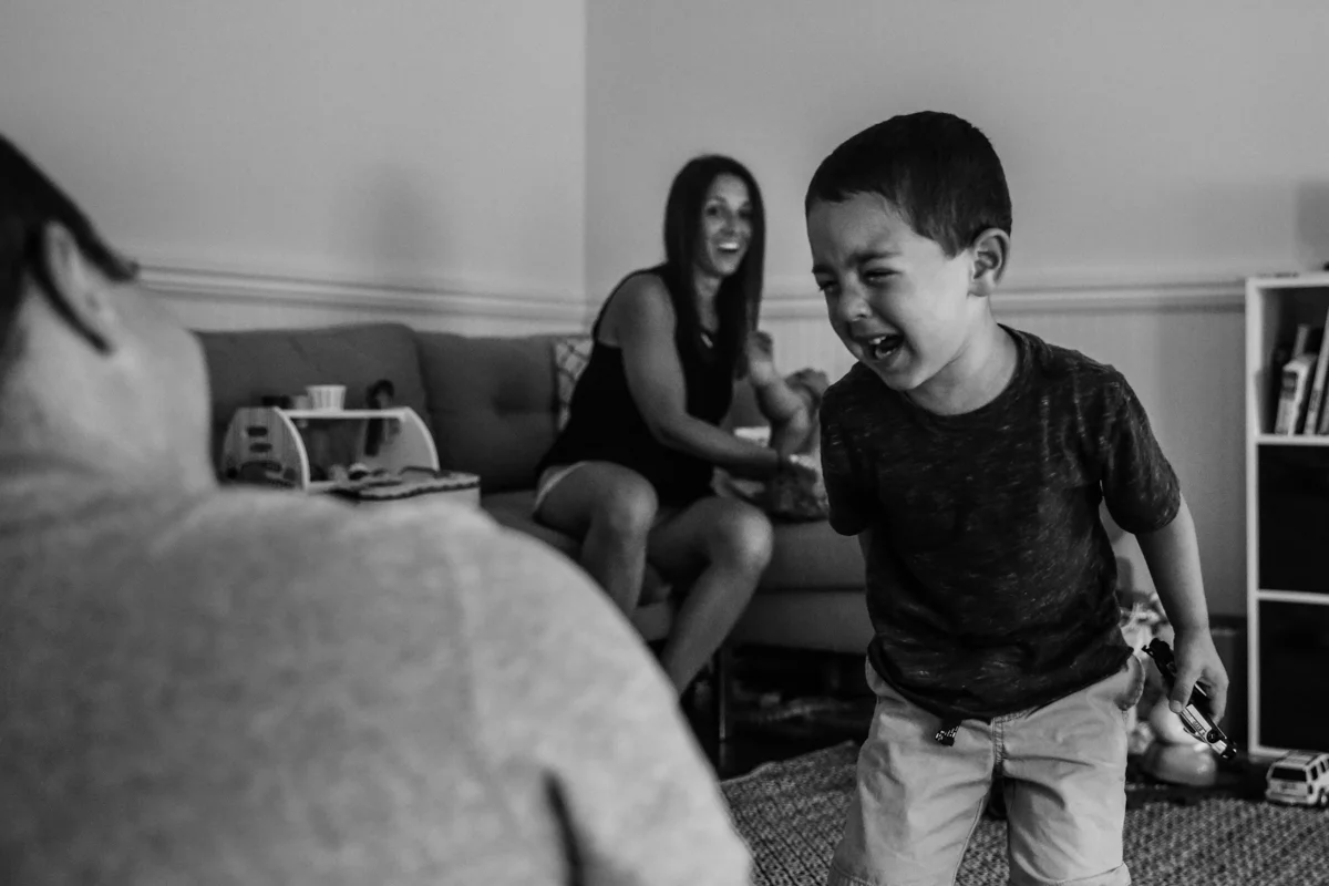 Boy holding a toy car cries while mom is surprised in the background