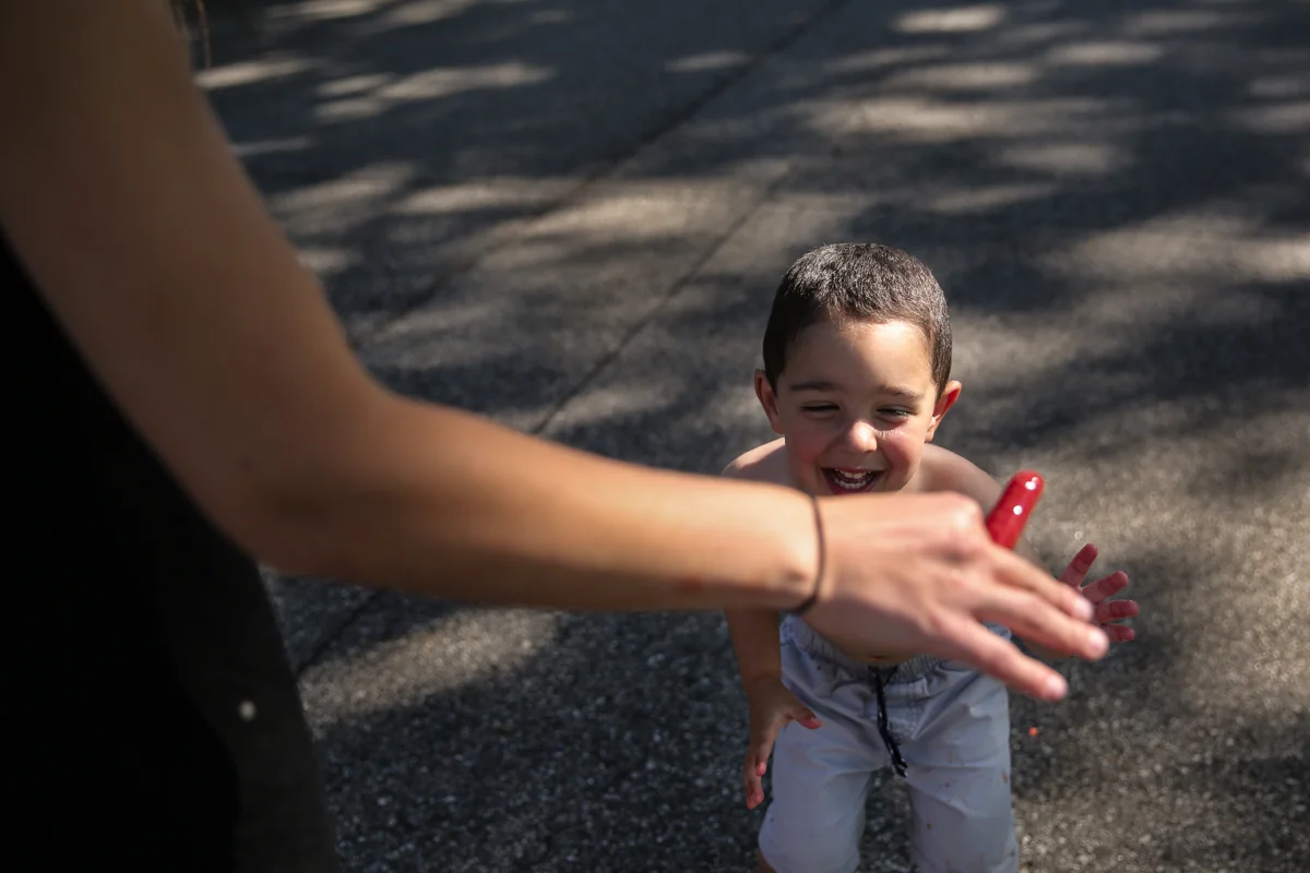 An arm holds a melting red ice pop while a boy tries to reach for it
