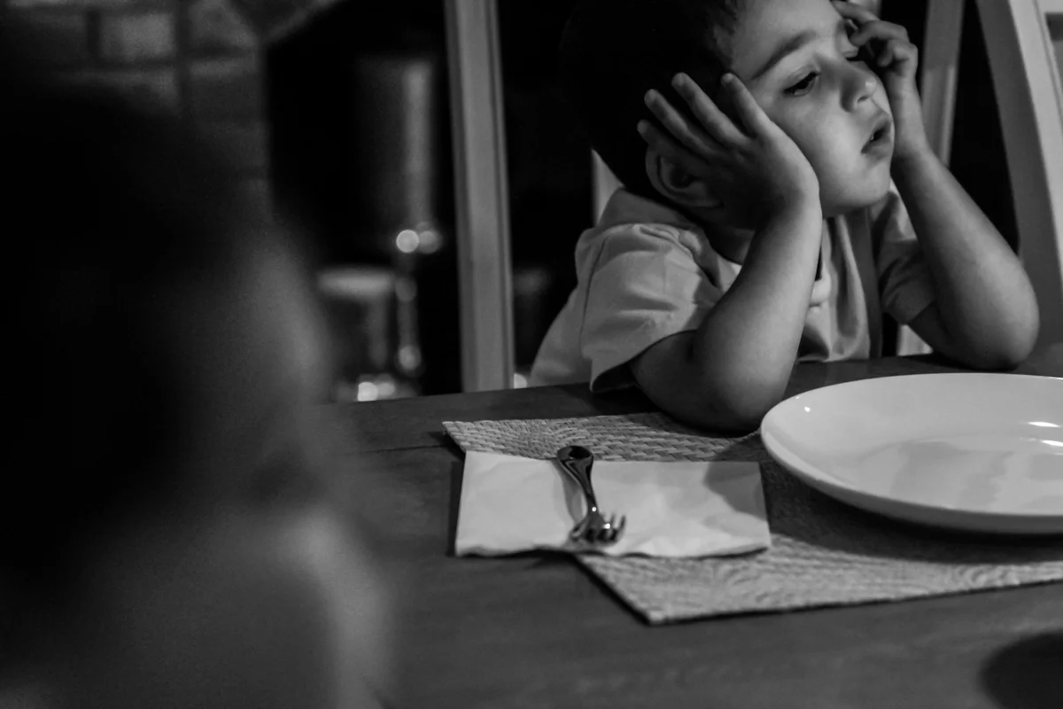 Tired boy rests head on hands at dining table