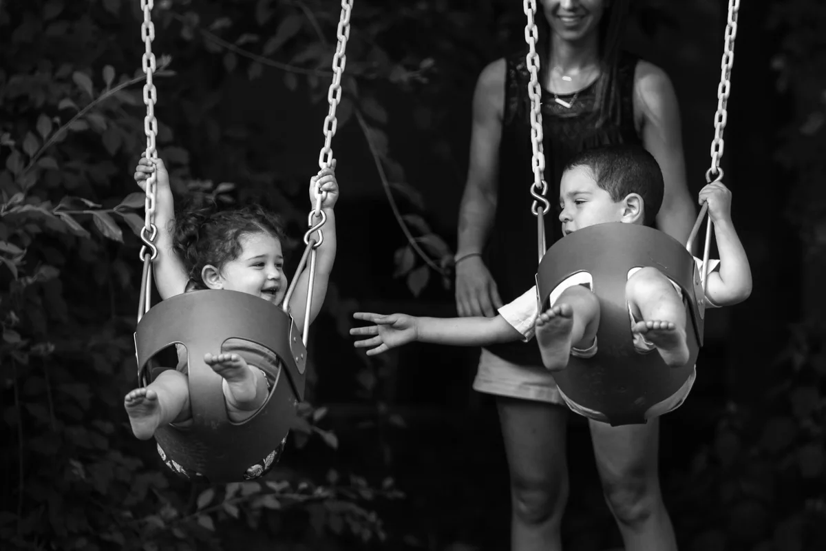 Boy seated in swing reaches out to girl seated in swing
