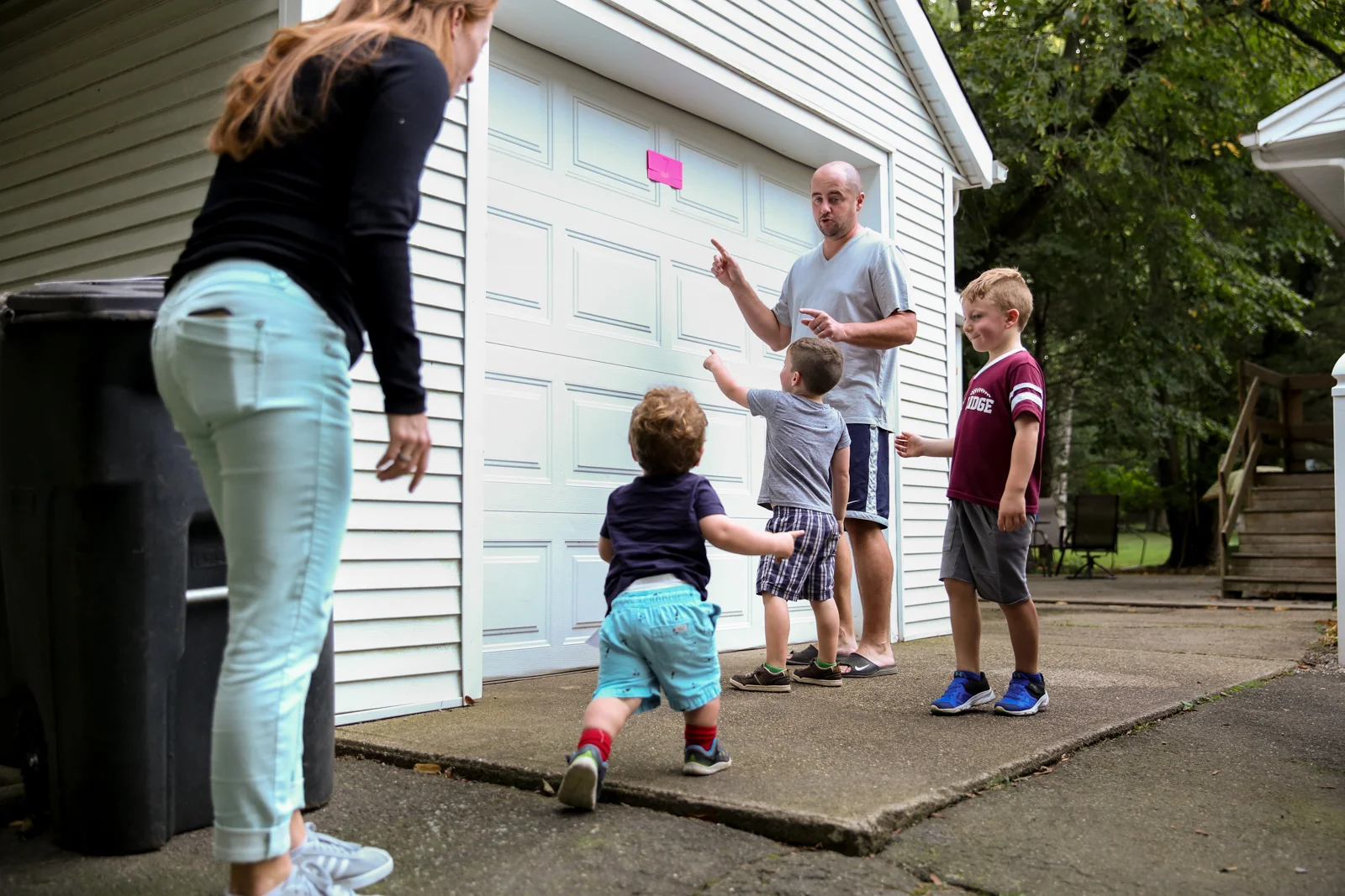 Man, woman, and three boys point to paper stuck up high on garage door