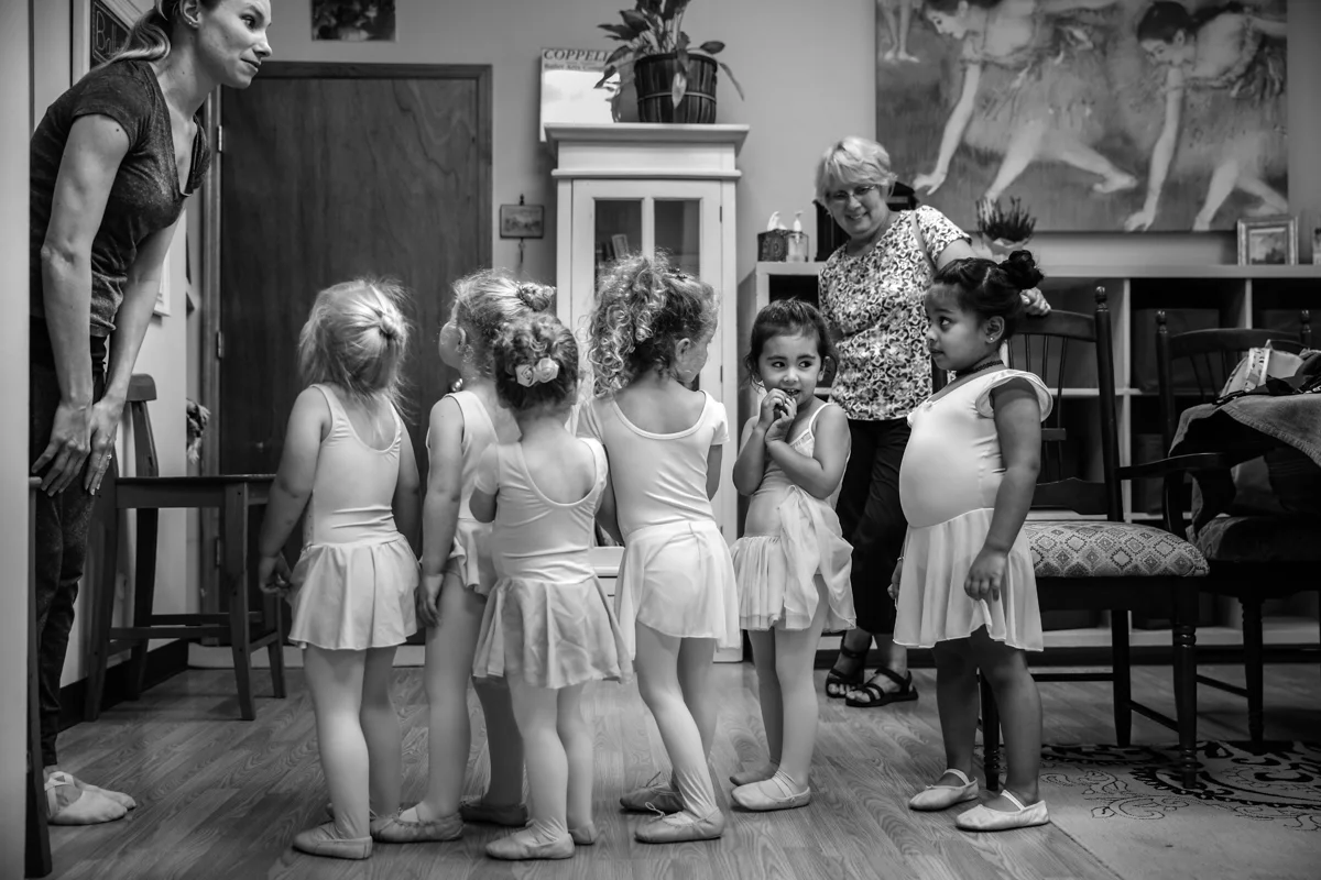 Girls wait nervously wait in line while teacher greats them before going into classroom.