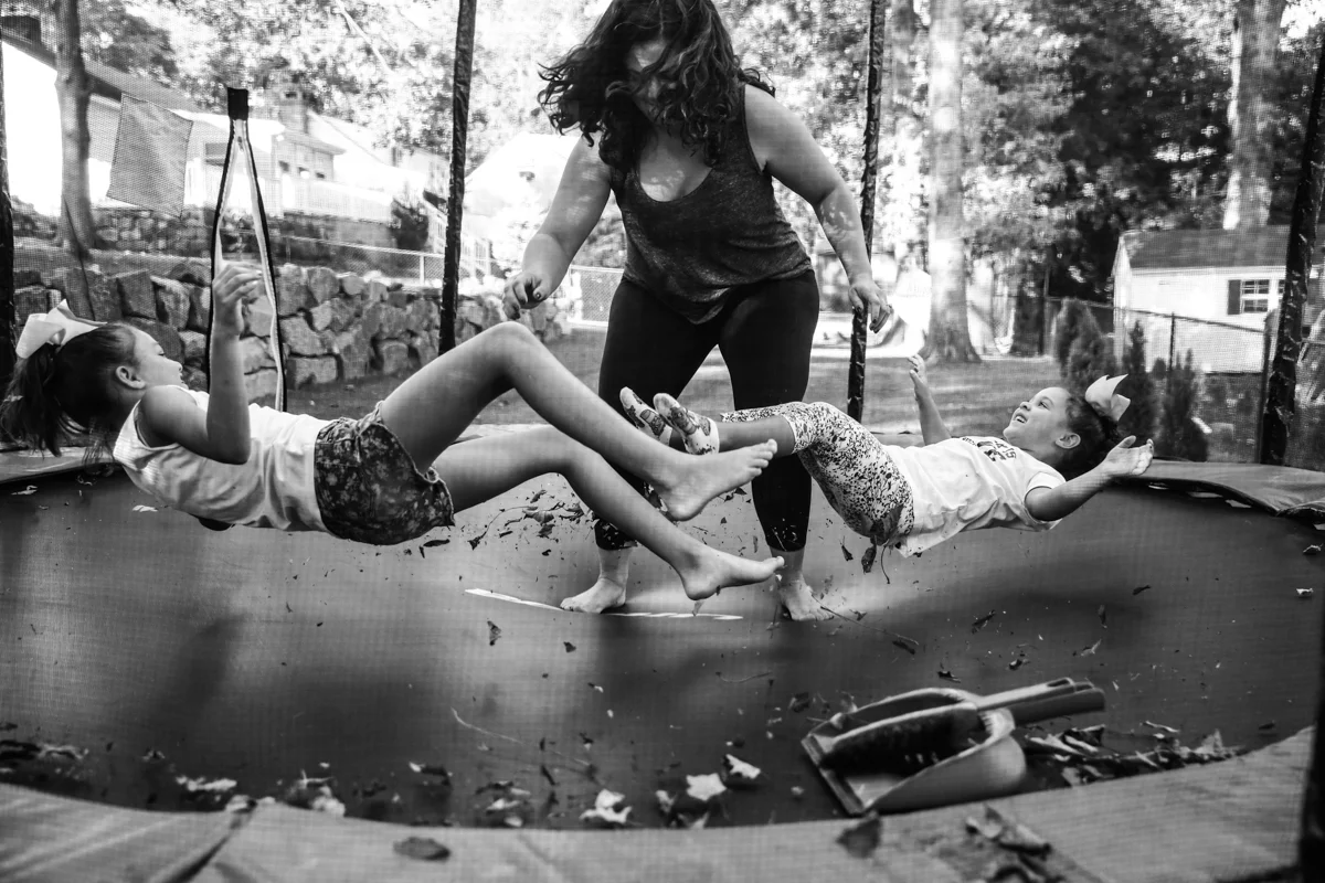 Woman jumps on trampoline making two girls lying down jump up