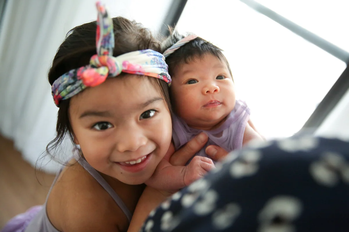 Girl smiles next to baby sisterM