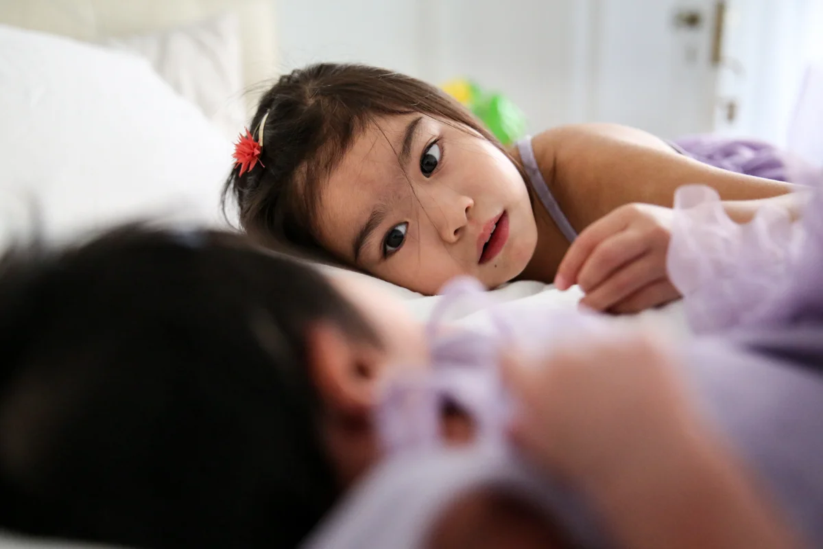 Girl lays on bed looking at her baby sister