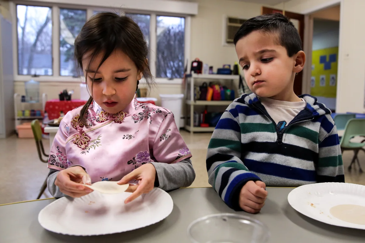 Girl wraps dumpling on a plate while boy looks over skeptically
