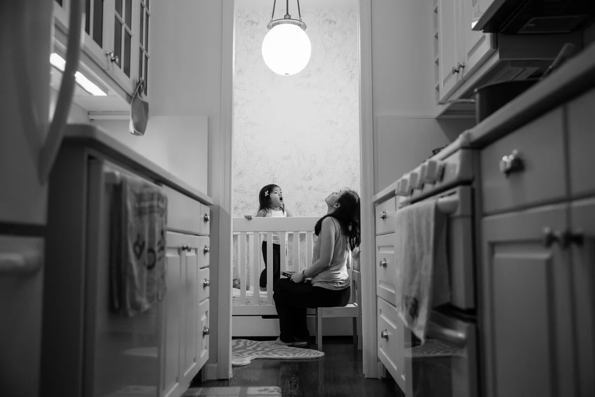 Girl stands in crib while woman sits in chair3
