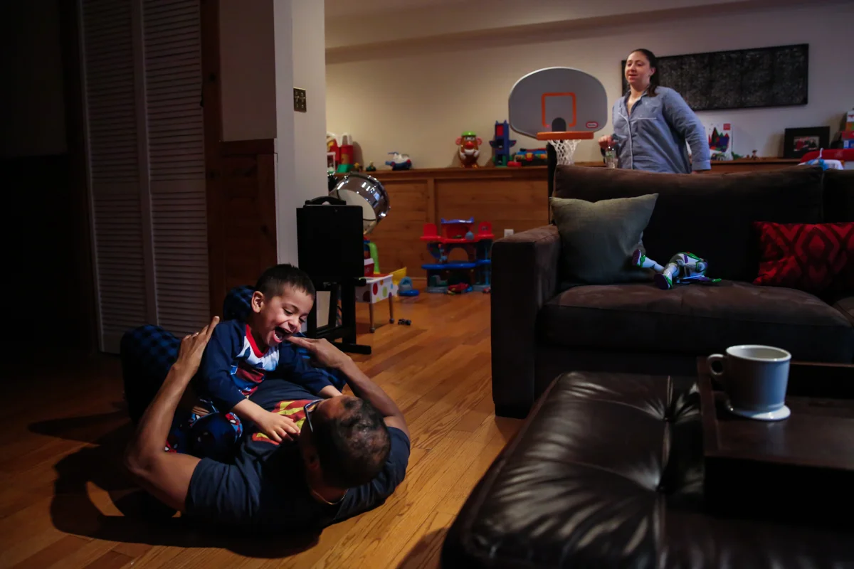 Boy and father wrestle on floor while woman walks behind couch