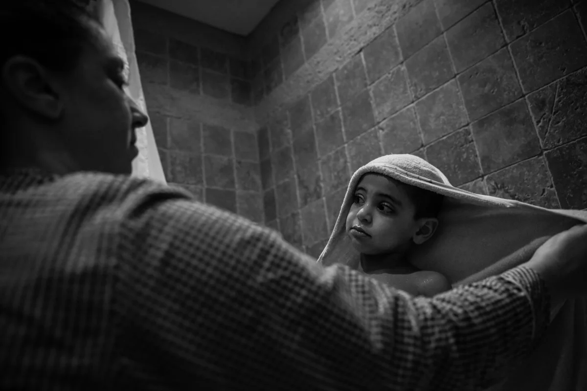 Boy wrapped in towel looks up at mother while standing in tub