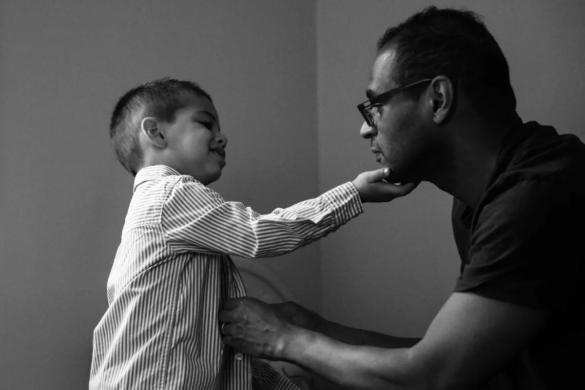 Boy holds man's chin while man buttons boy's shirt