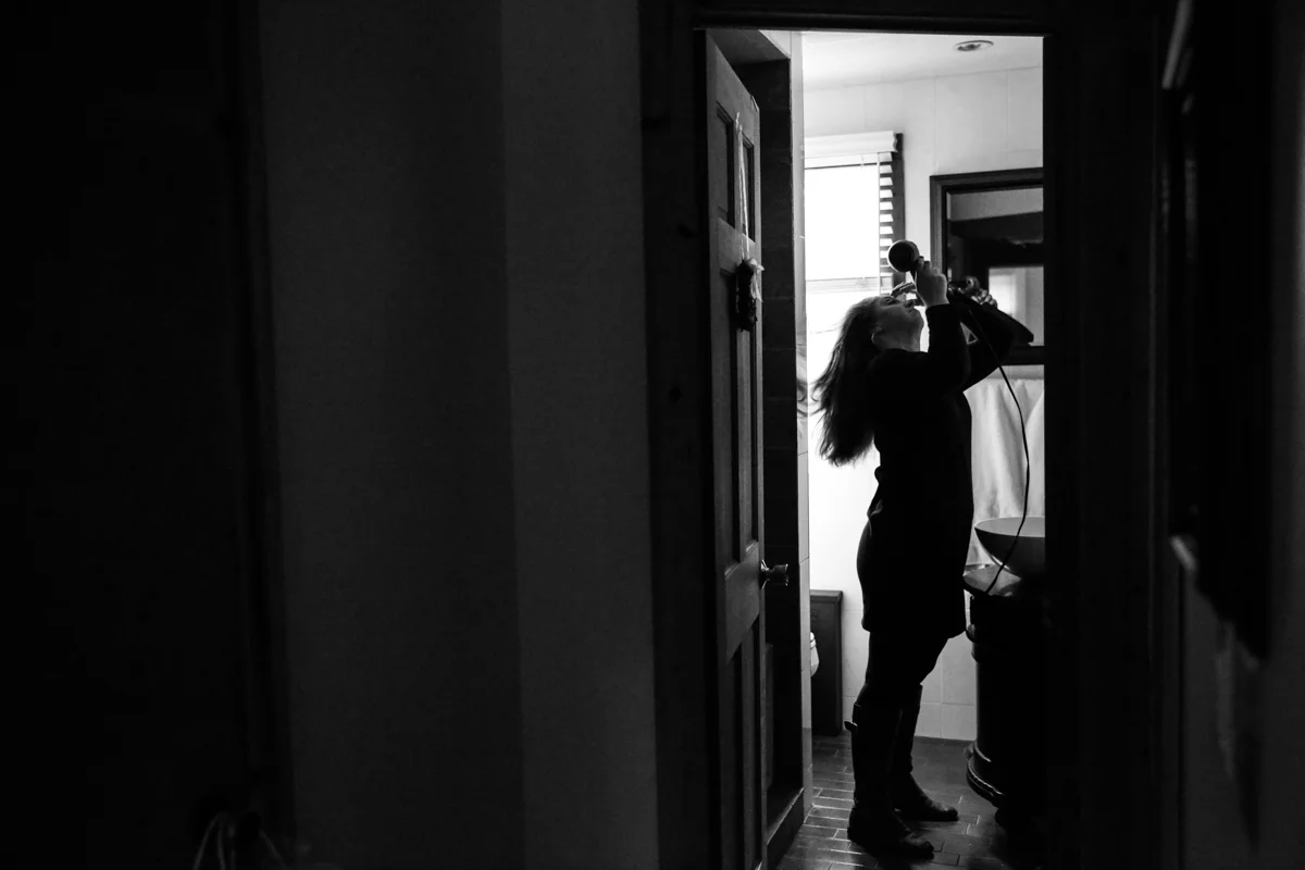 Woman blowdries her hair while standing in bathroom doorway