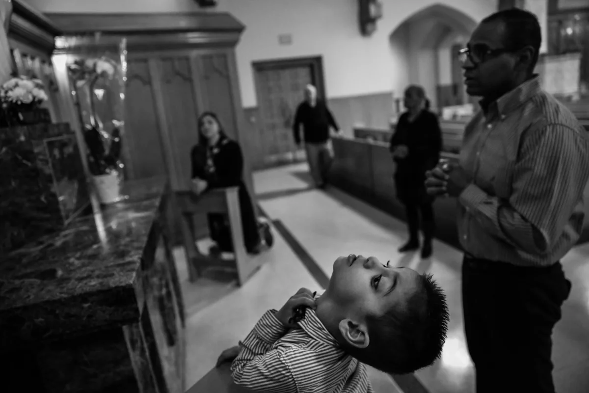 Boy grabs his collar while family members pray