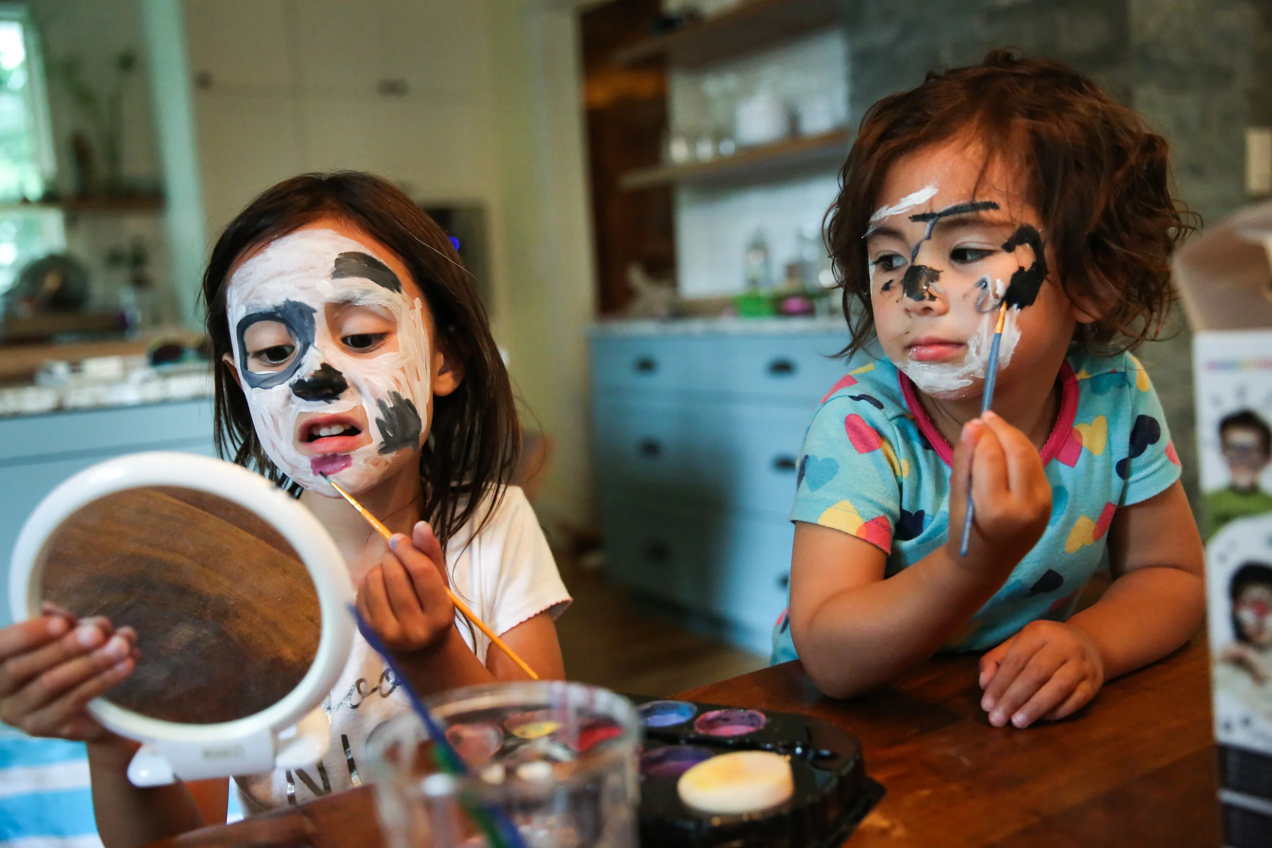 Two kids painting faces at table
