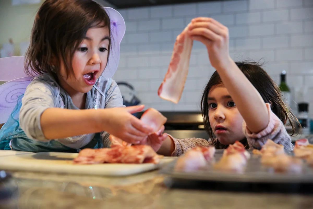 Two girls prepares bacon on a baking sheet