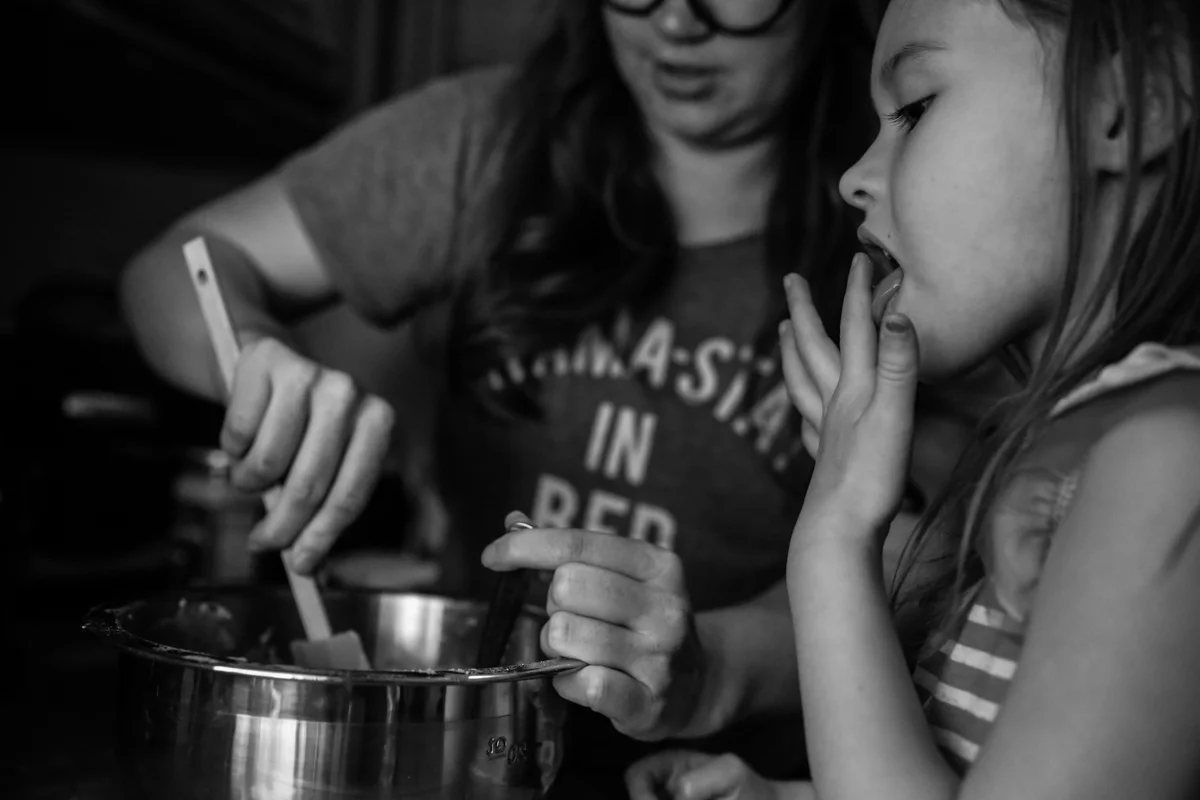 Girl licks finger while woman stirs contents of bowl