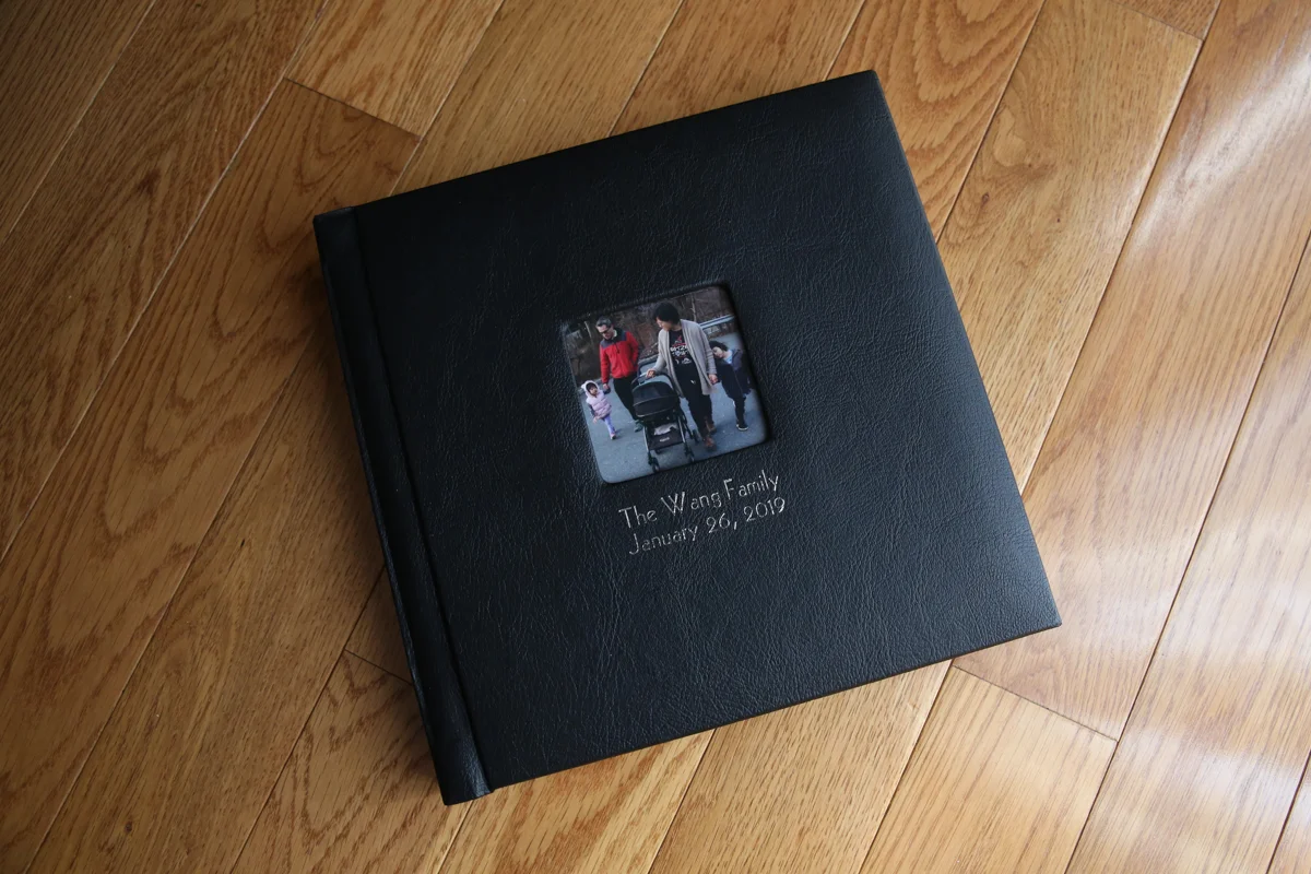 Black leather photo album with image of family, on a wood floor