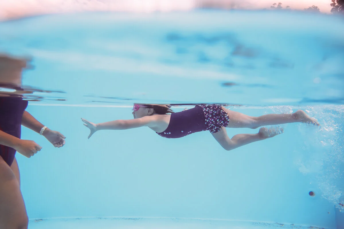 Girl swims underwater reaching her hand out to swim instructor