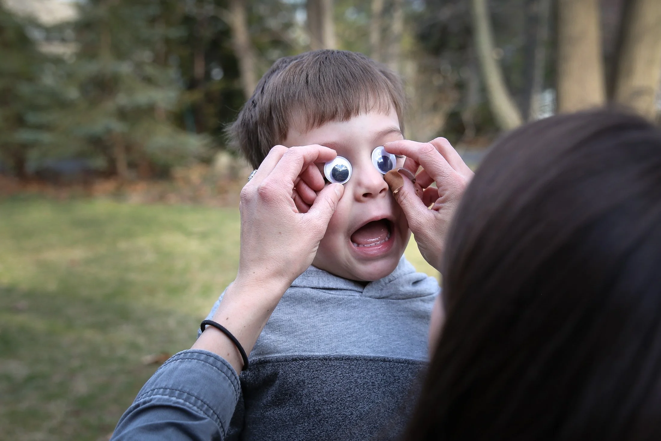 a parent holds up large googly eyes over the eyes of a young boy. young boy reacts with excitement
