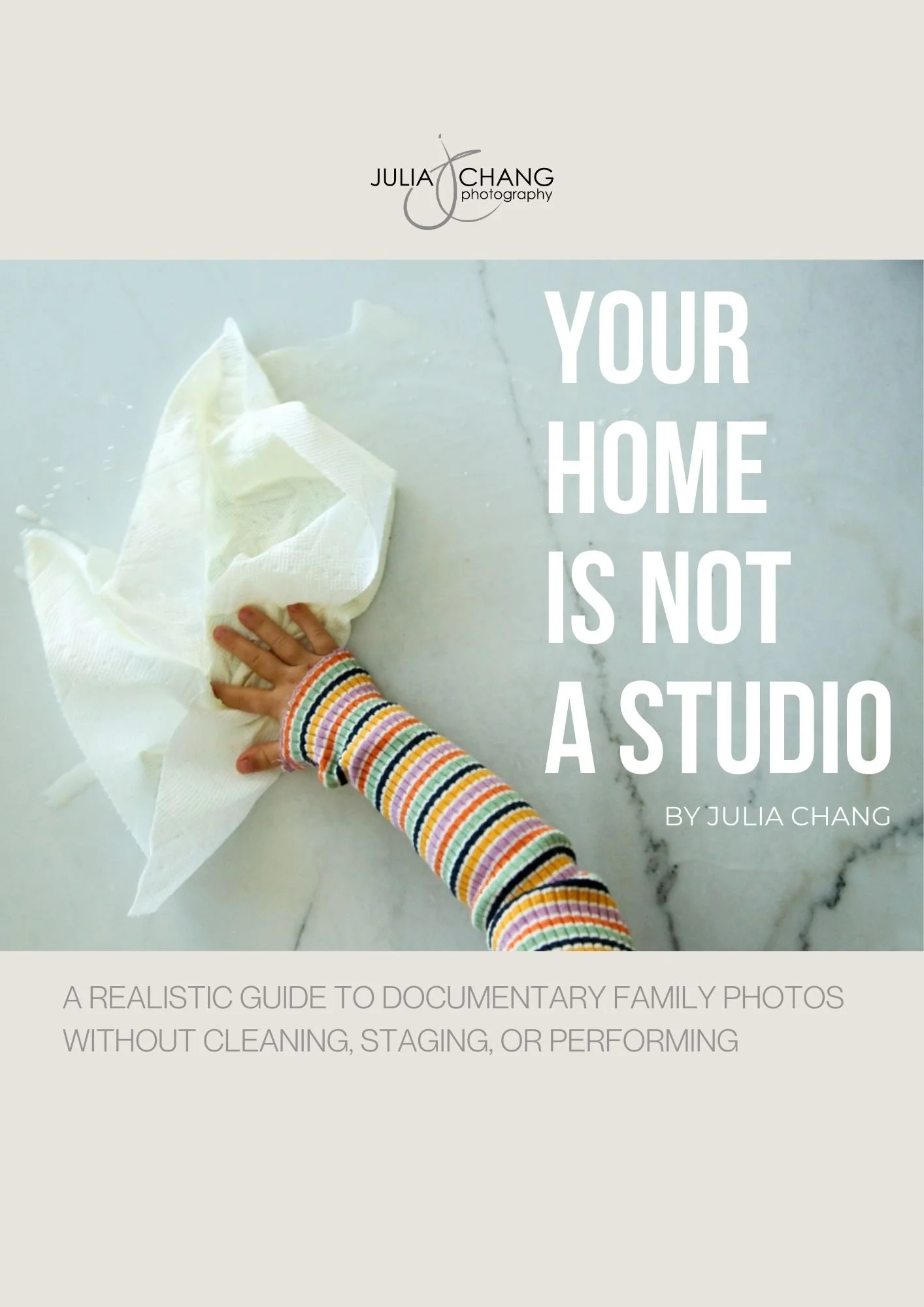 a child's hand wiping milk off a marble counter top with a paper towel, overlay text of "your home is not a studio, a realistic guide to documentary family photos without cleaning, staging, or performing, by Julia Chang"