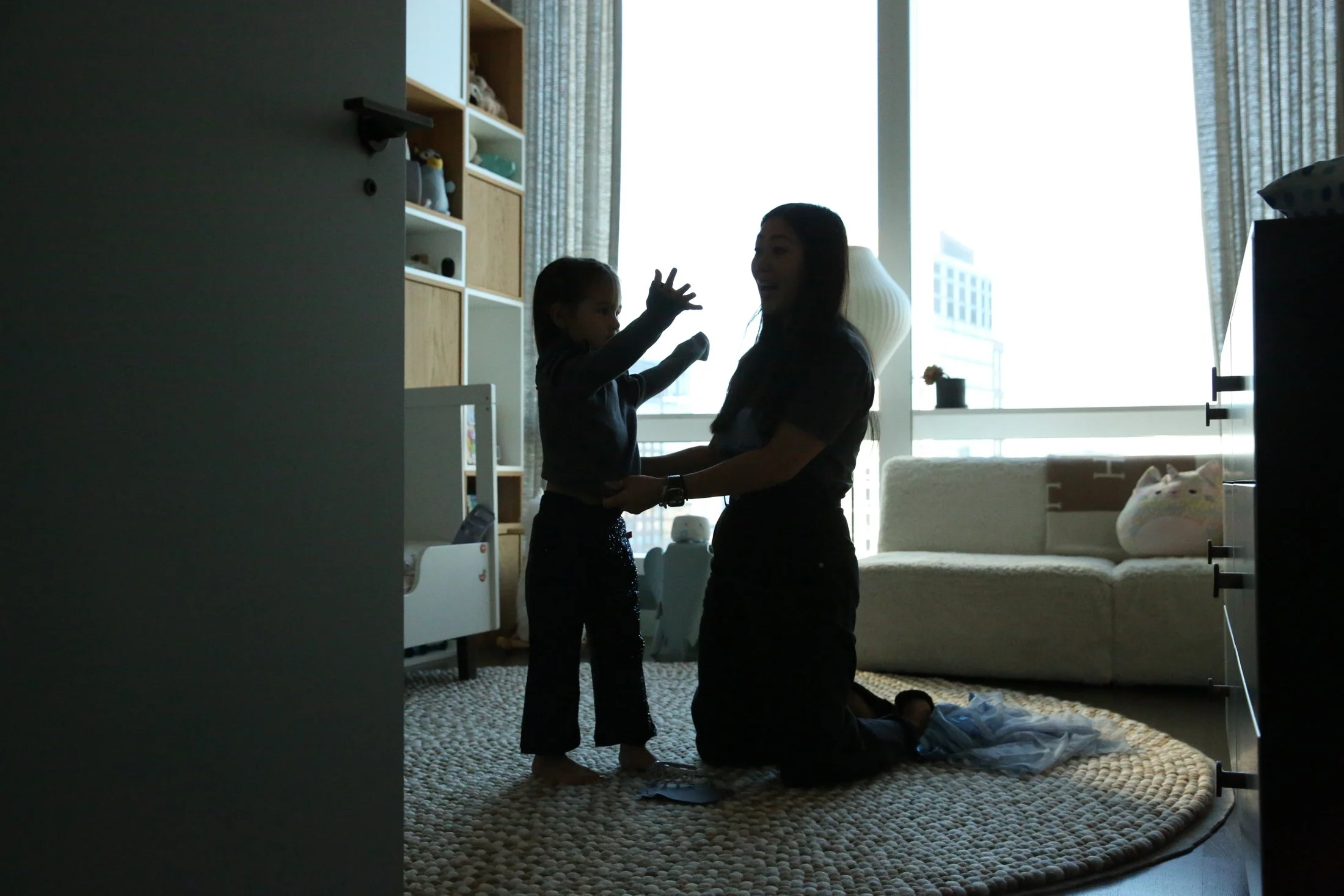silhouette of mother helping daughter get dressed. girl stretching arms through sleeves