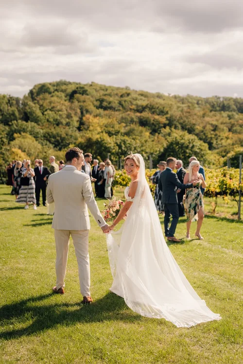 A newly married couple holding hands at an outdoor vineyard ceremony