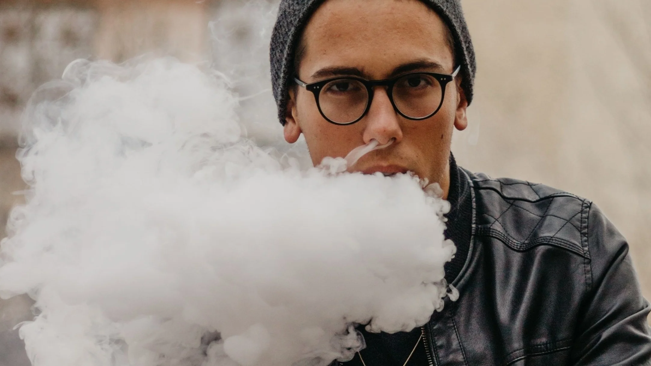 Photo of young man vaping, with vapor in a huge cloud emerging from his mouth and nose, almost covering his face.