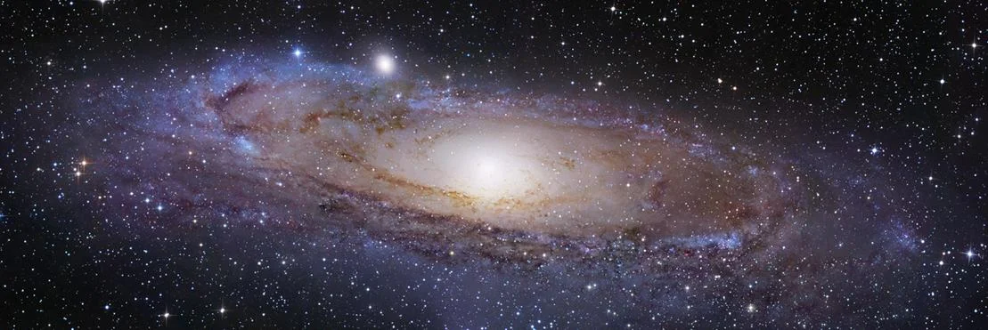 Wide view of a galaxy with bright center, surrounded by stars and cosmic dust.
