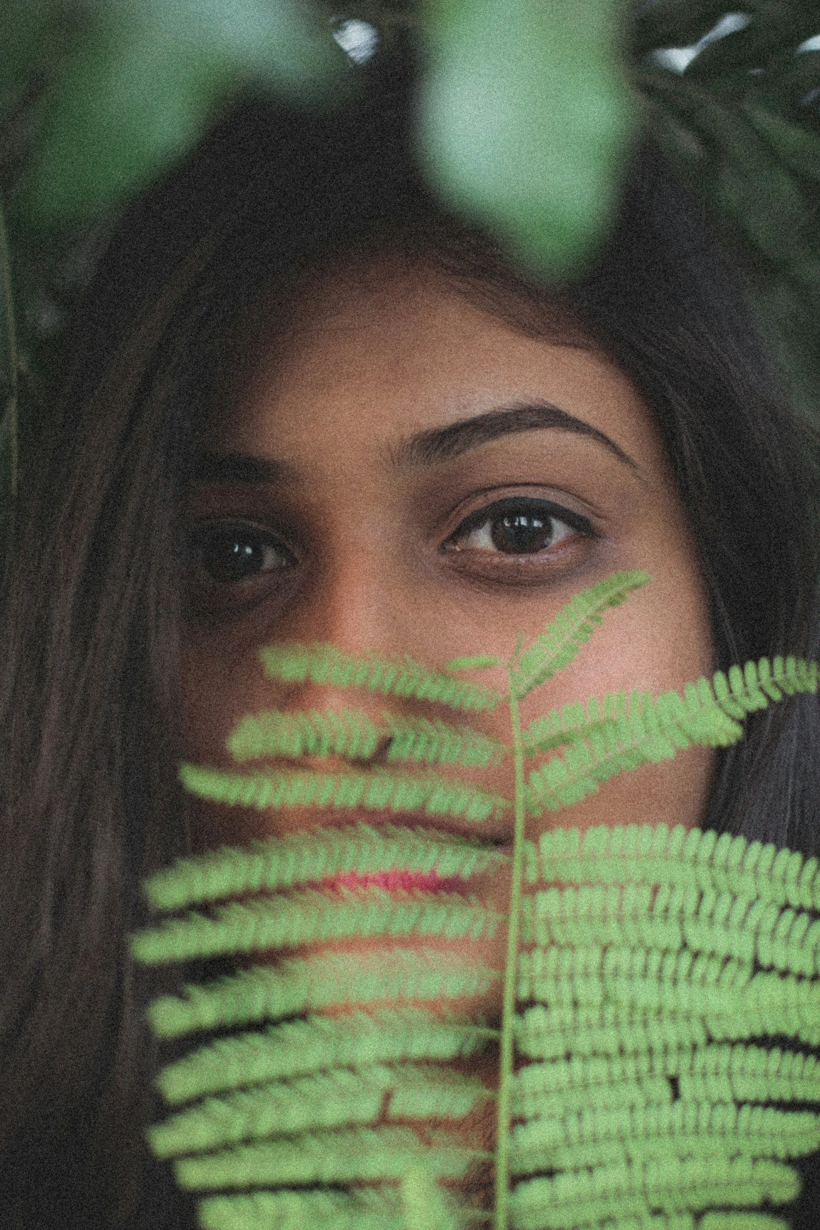Close-up of a woman's face with a green fern leaf partially covering her mouth