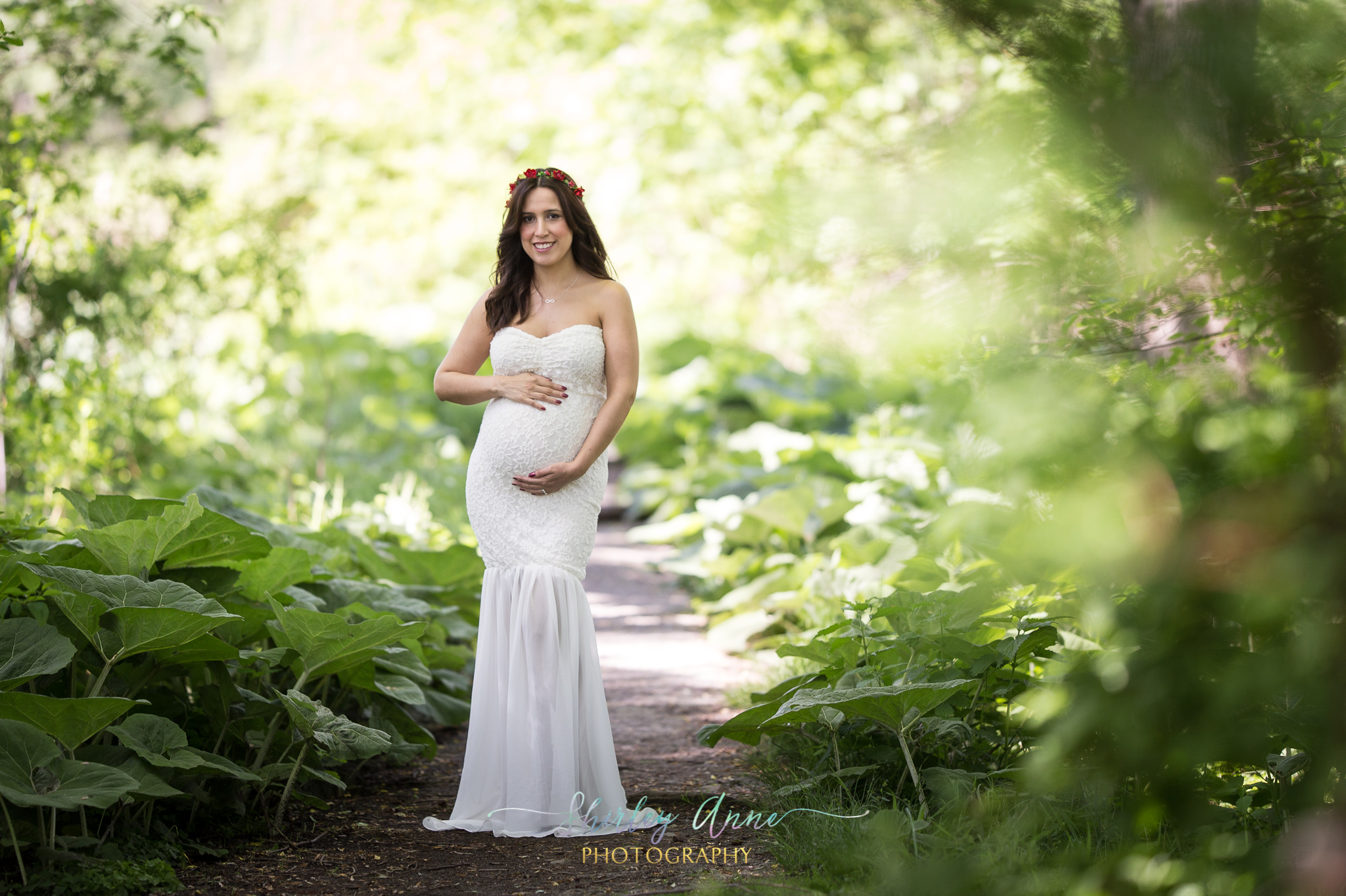 expecting mom in green forest during outdoor session in maternity gown